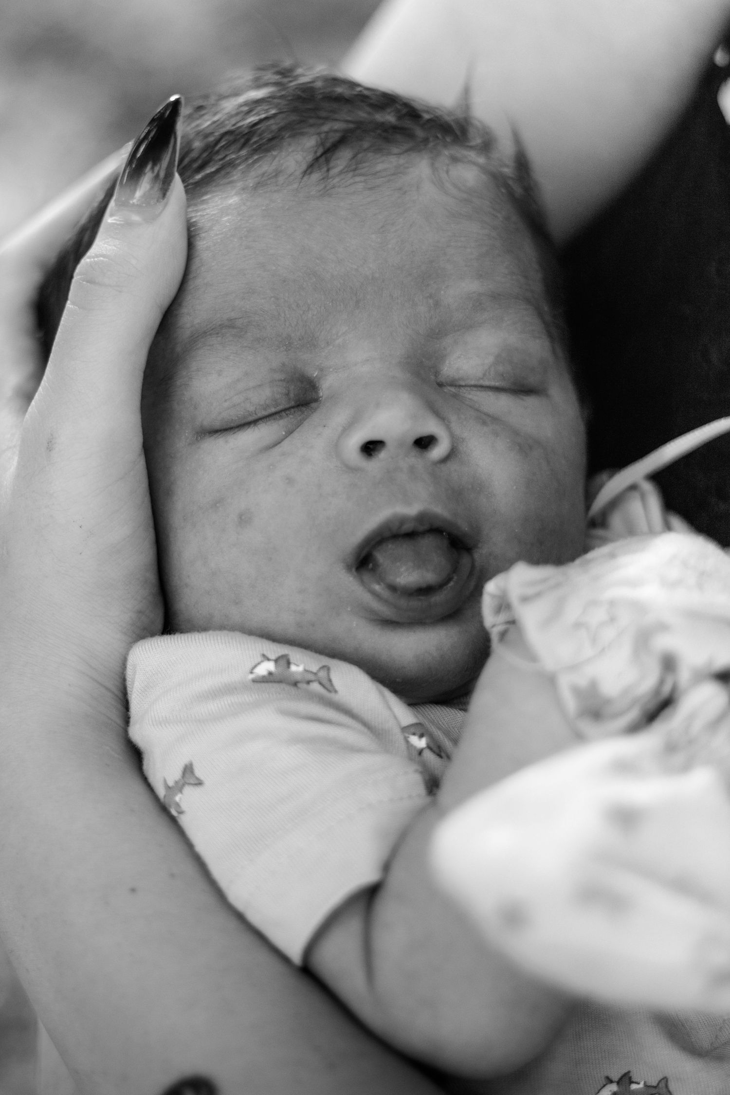 Black and white photo of a sleeping newborn baby cradled in a mother's hands, mouth slightly open.