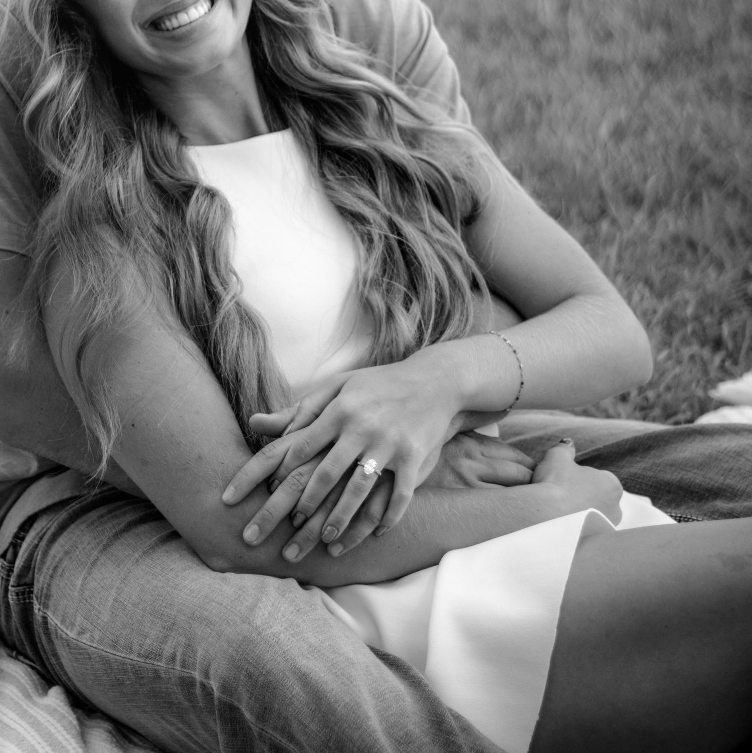 Black and white photo of a couple sitting together, holding hands, showcasing an engagement ring on the woman's finger.