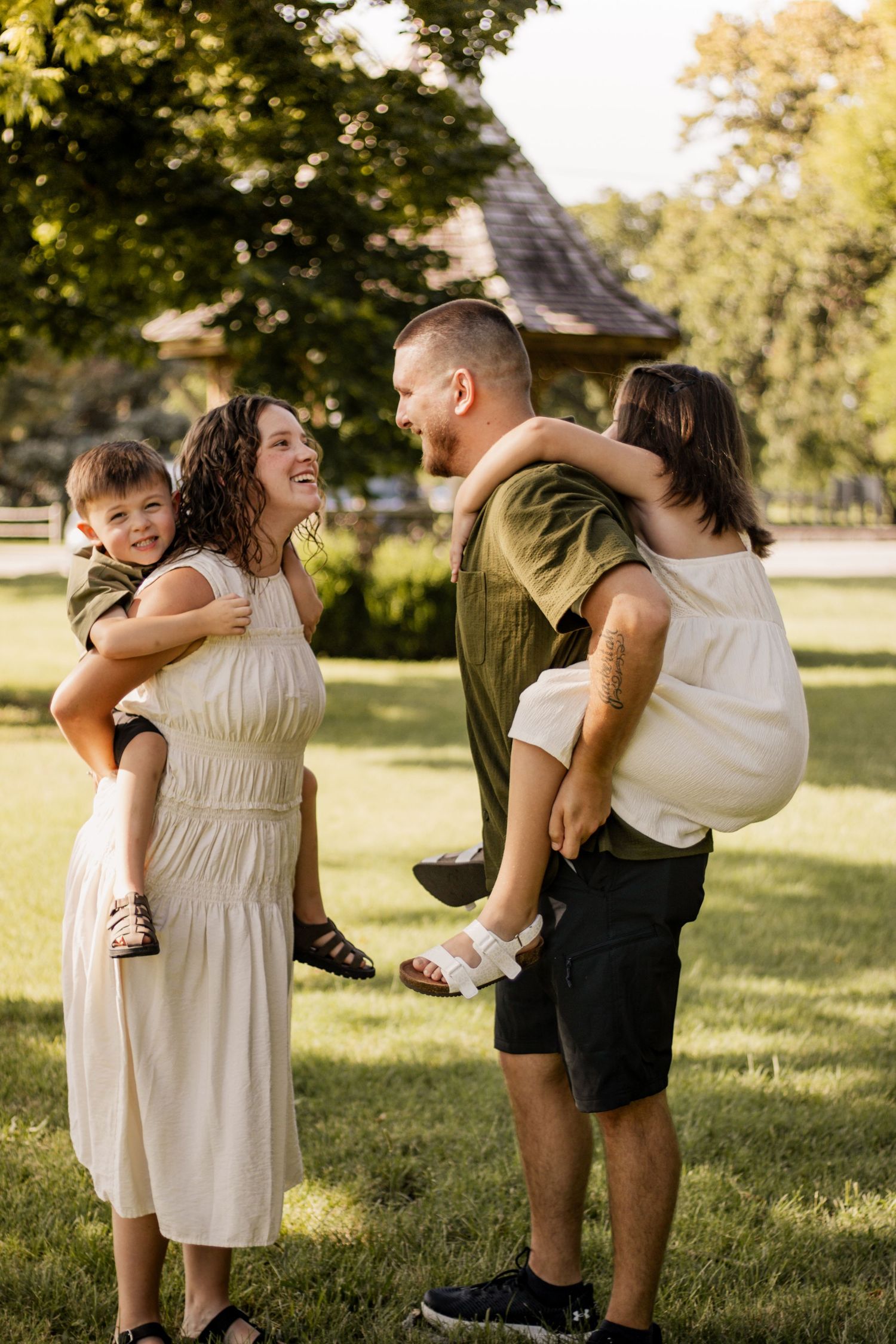 Happy family of four enjoying a sunny day outdoors, parents carrying children on their backs.