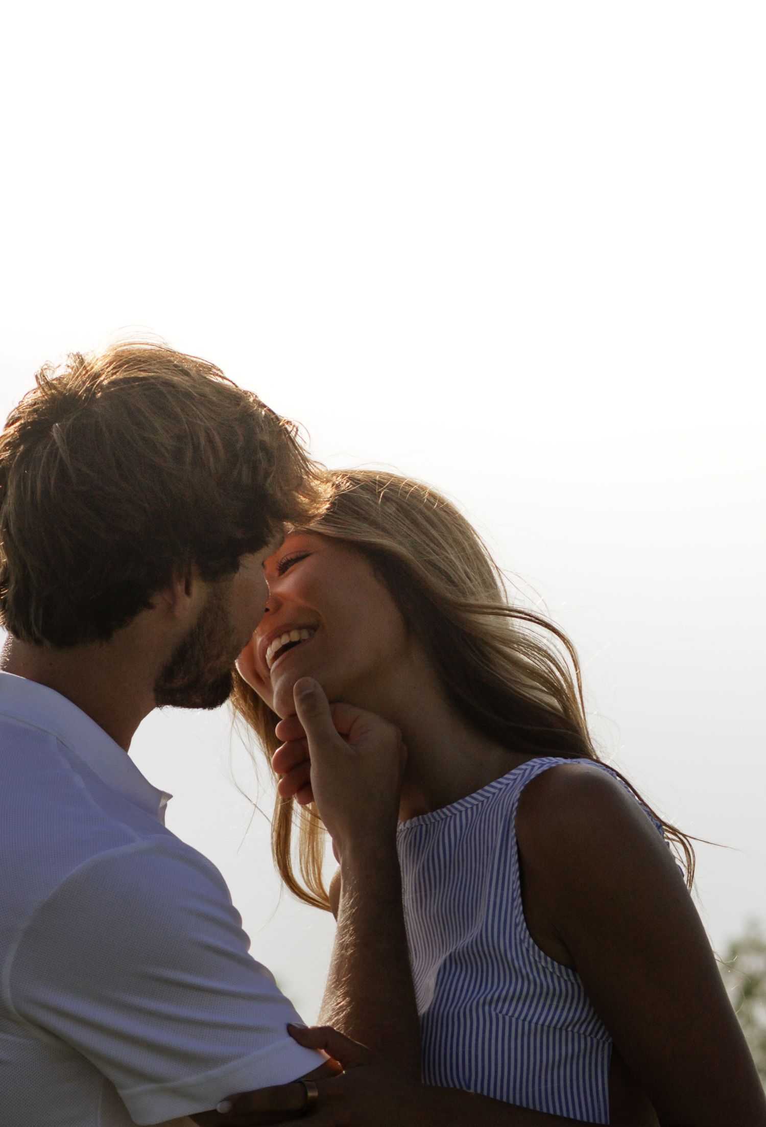 A romantic couple sharing an intimate moment outdoors, the man tenderly touching the smiling woman's face in golden light.