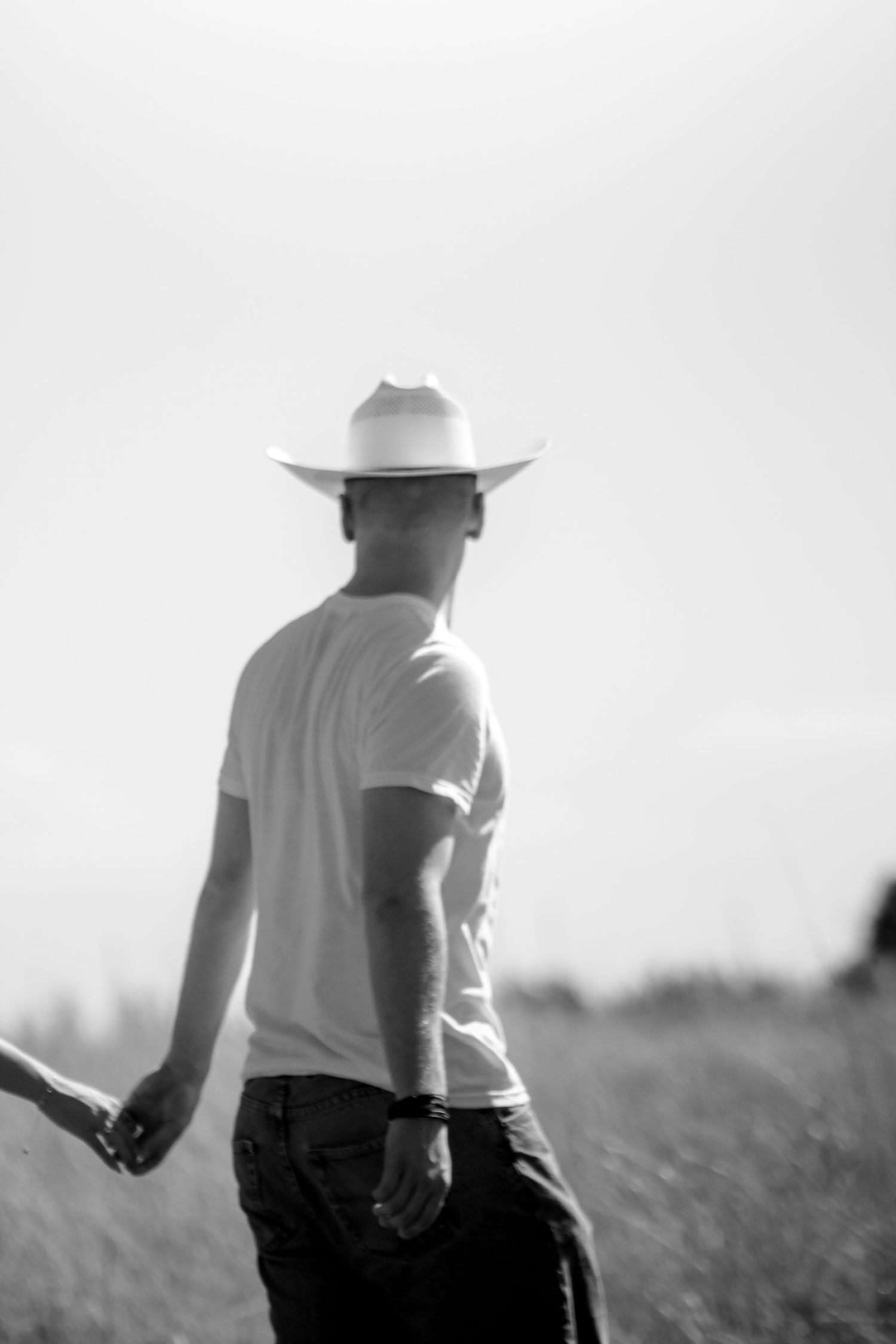 Black and white photo of a man in a white cowboy hat and t-shirt walking through an open field.