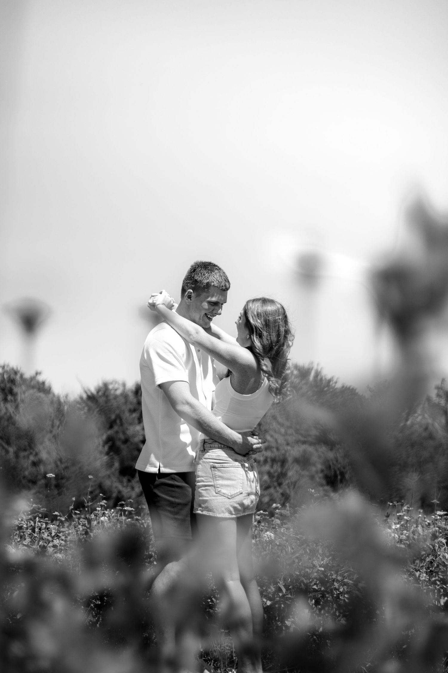 Black and white photo of a couple embracing romantically in a lush flower field.