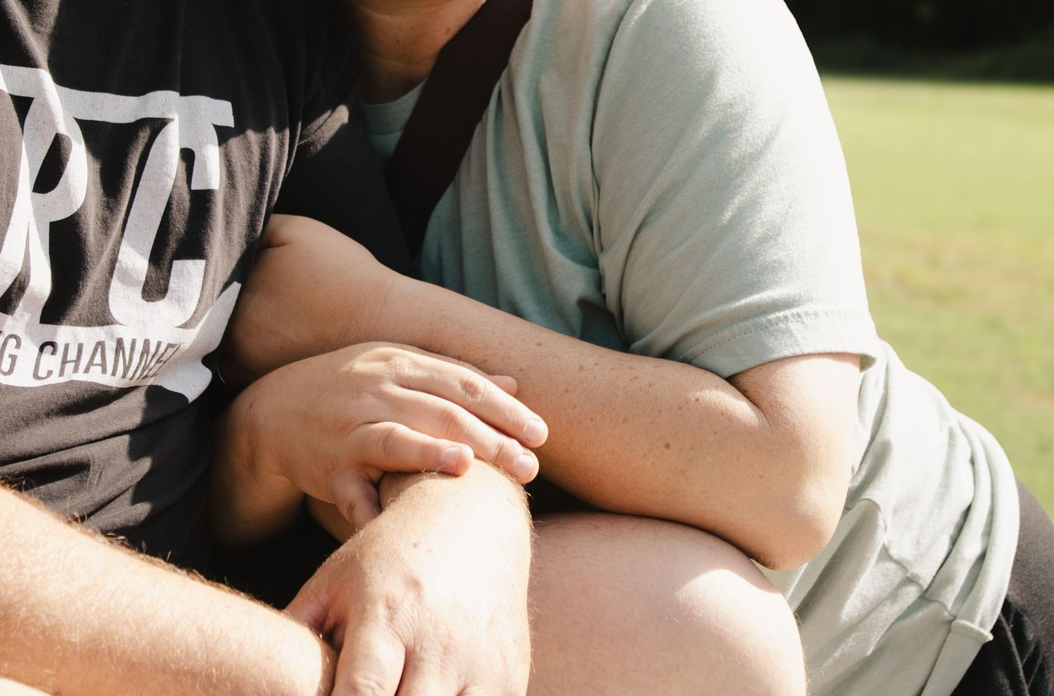 Close-up of couple holding hands affectionately while sitting together outdoors in a park.