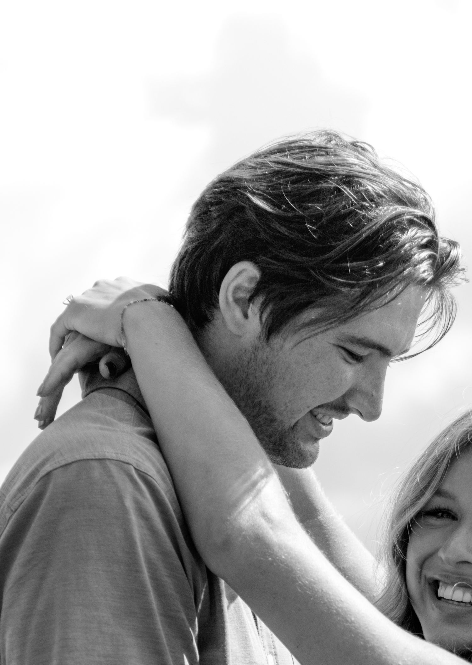 Black and white photo of a smiling couple embracing outdoors, woman resting arms on mans shoulders.