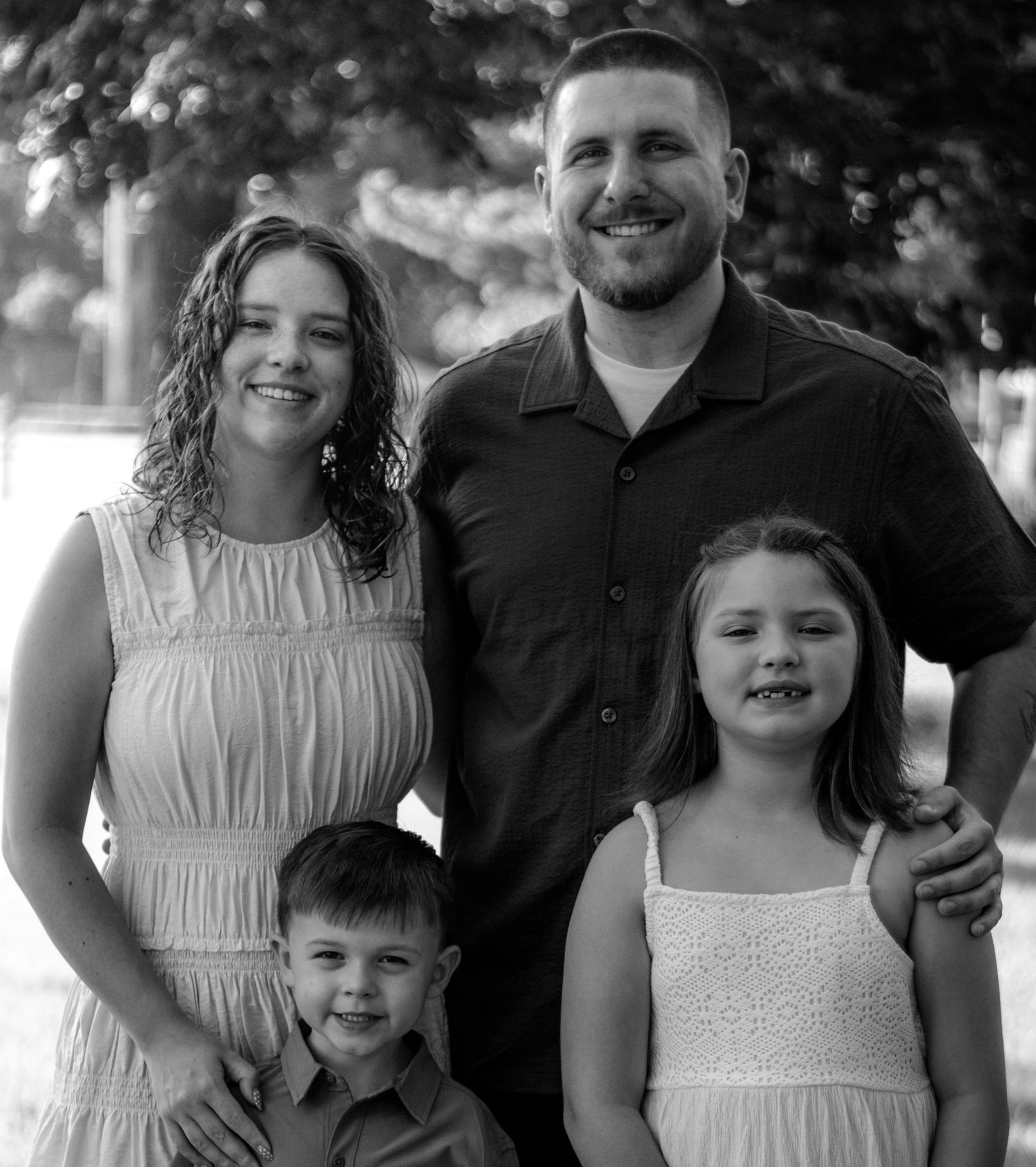 Black and white family portrait of smiling parents with two young children outdoors.