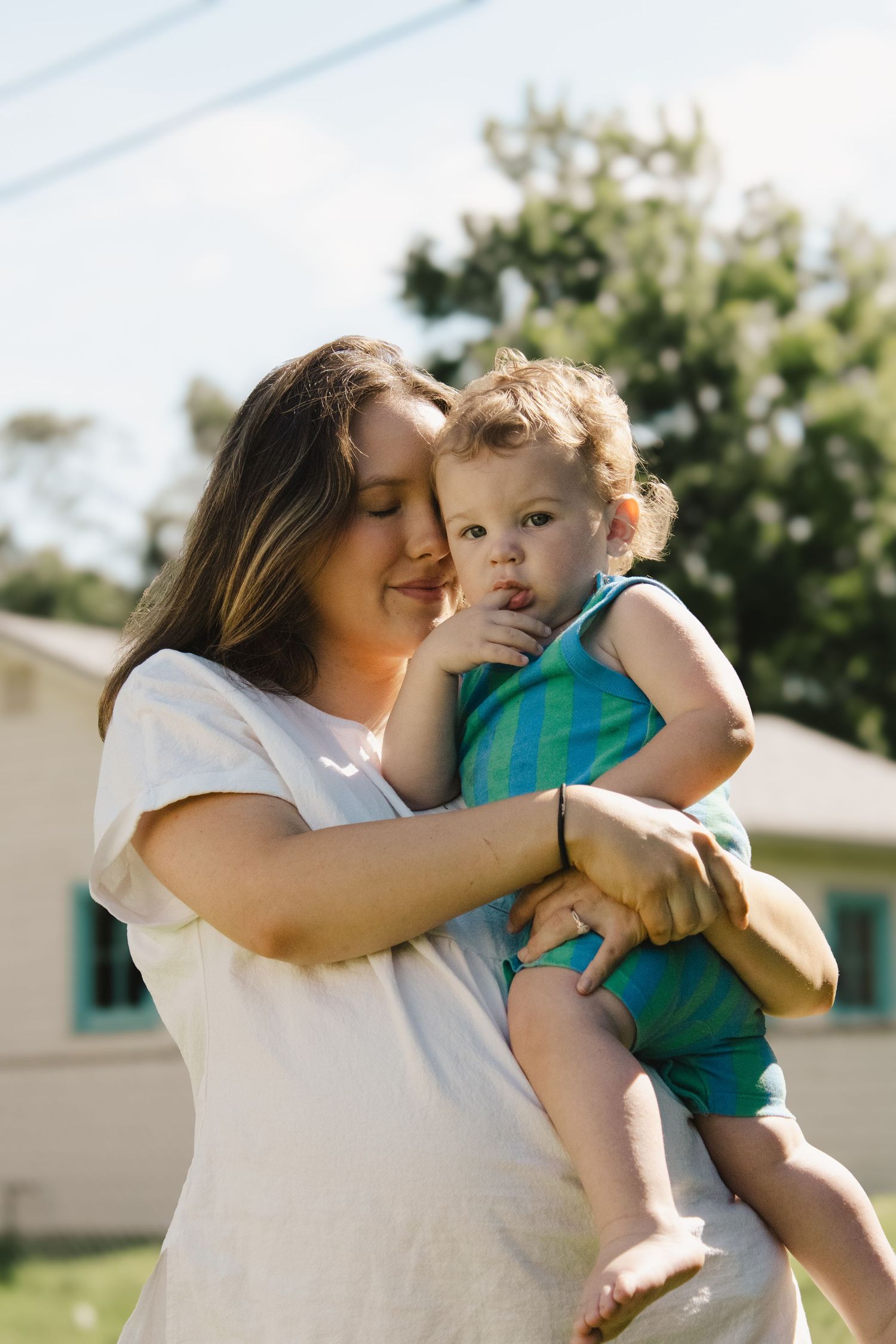 Pregnant woman tenderly holding a young toddler in blue outfit outside.