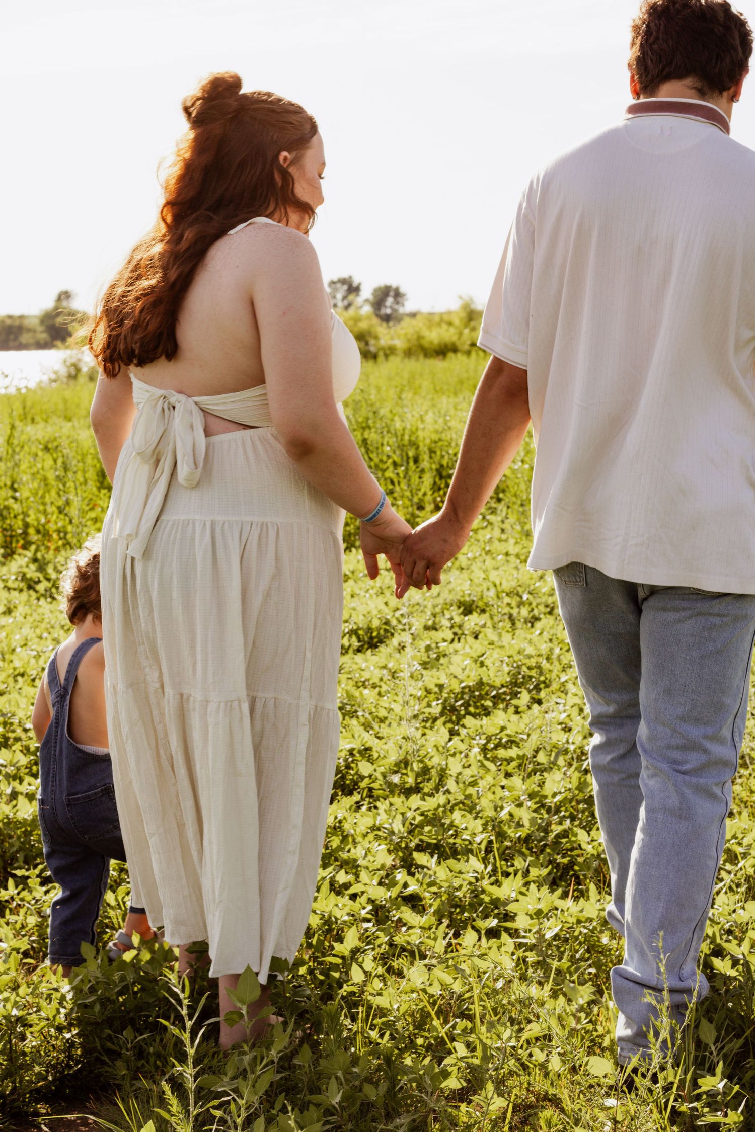 A couple holds hands in a green field while a child plays nearby on a sunny day.