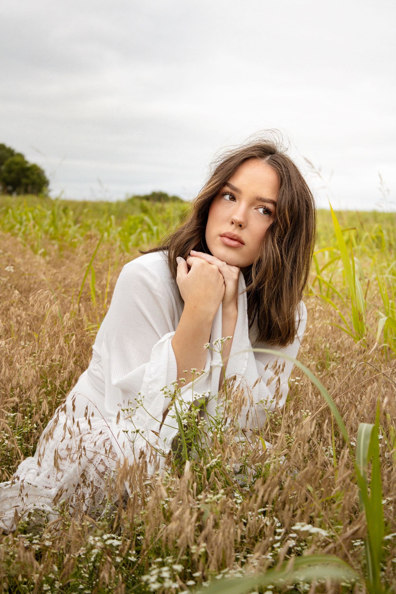 Young woman in white dress lying in tall golden grass field looking thoughtfully away.