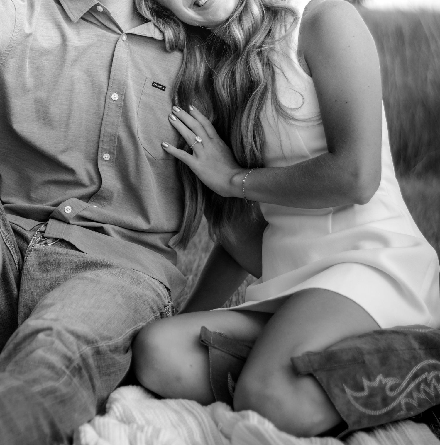 Black and white photo of a couple sitting closely together, woman in white dress resting hand on mans chest.