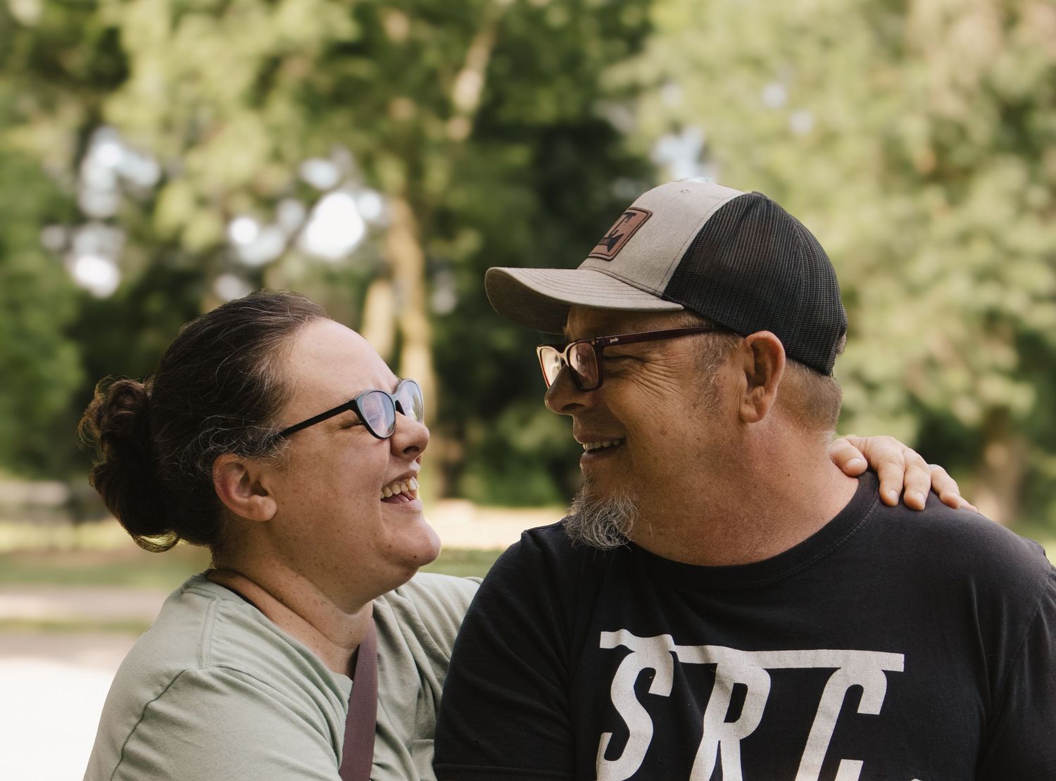 Couple smiling and looking at each other affectionately outdoors in a bright park setting.
