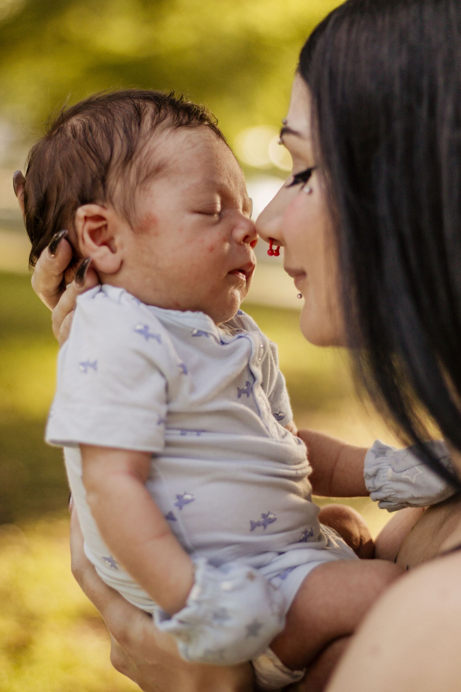 A mother tenderly holds her sleeping newborn baby outdoors, touching noses in a gentle moment of bonding.