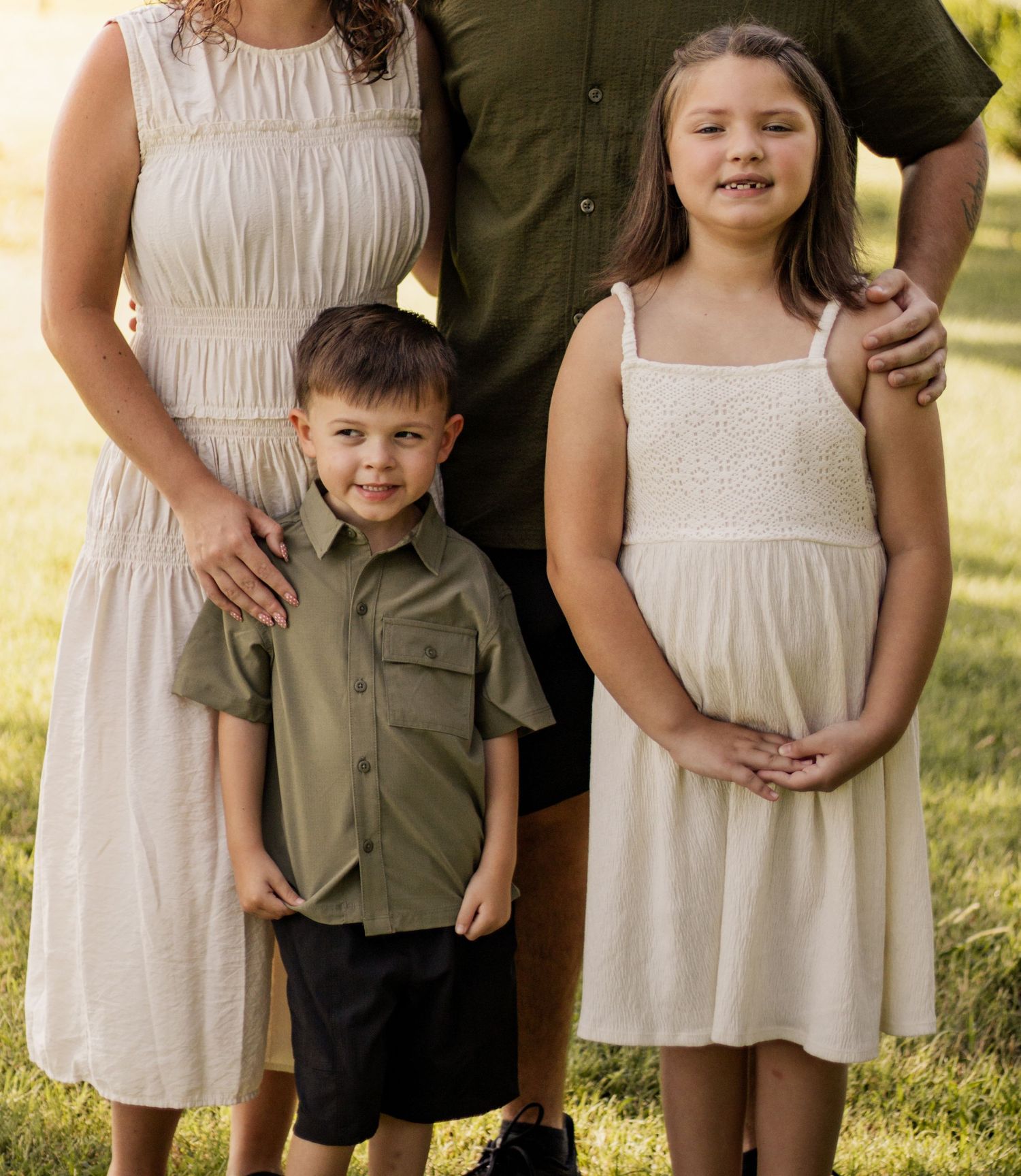 Family portrait with two adults and two children dressed in coordinating neutral and olive tones outdoors.