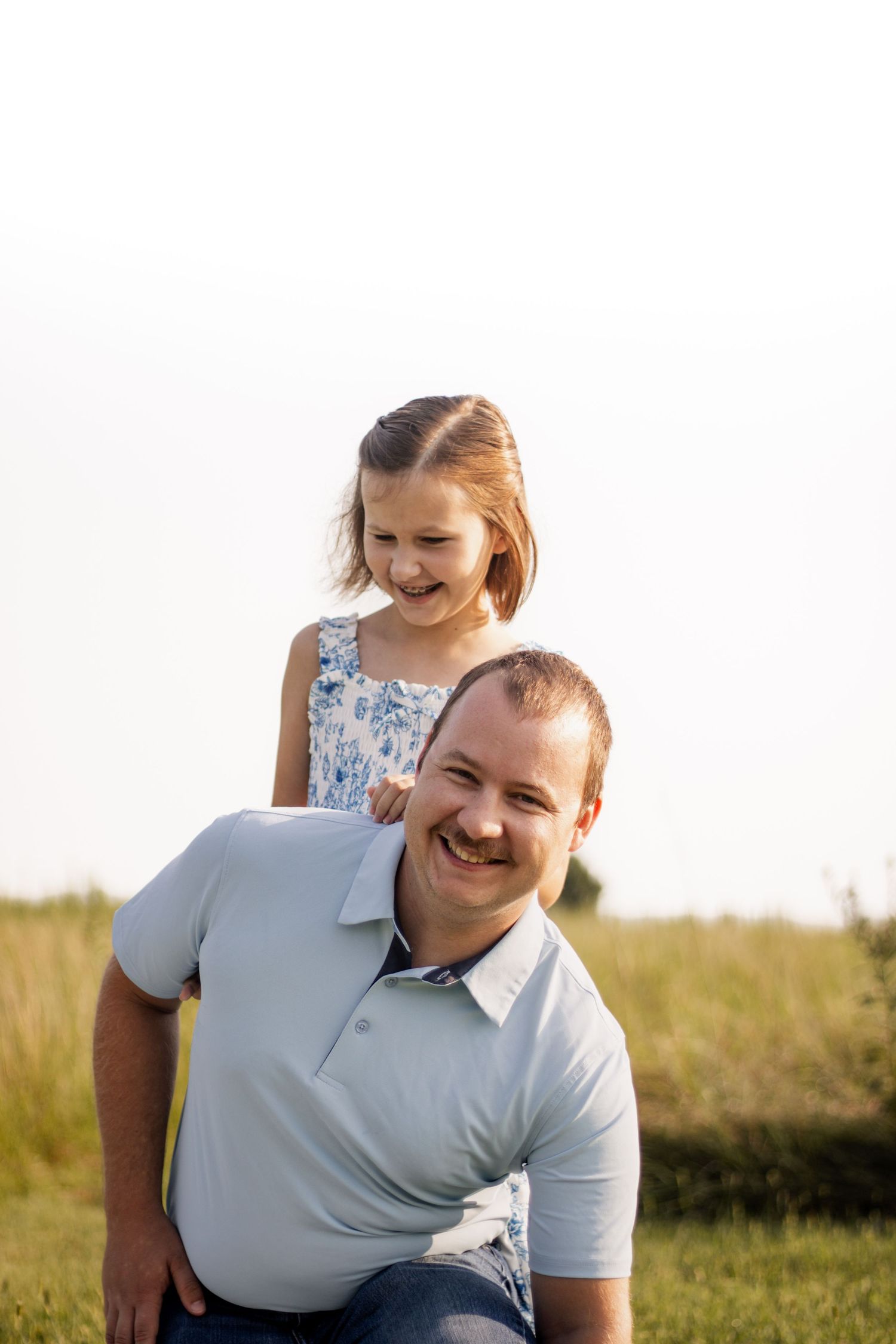 A happy father gives his laughing daughter a piggyback ride in a sunny field.