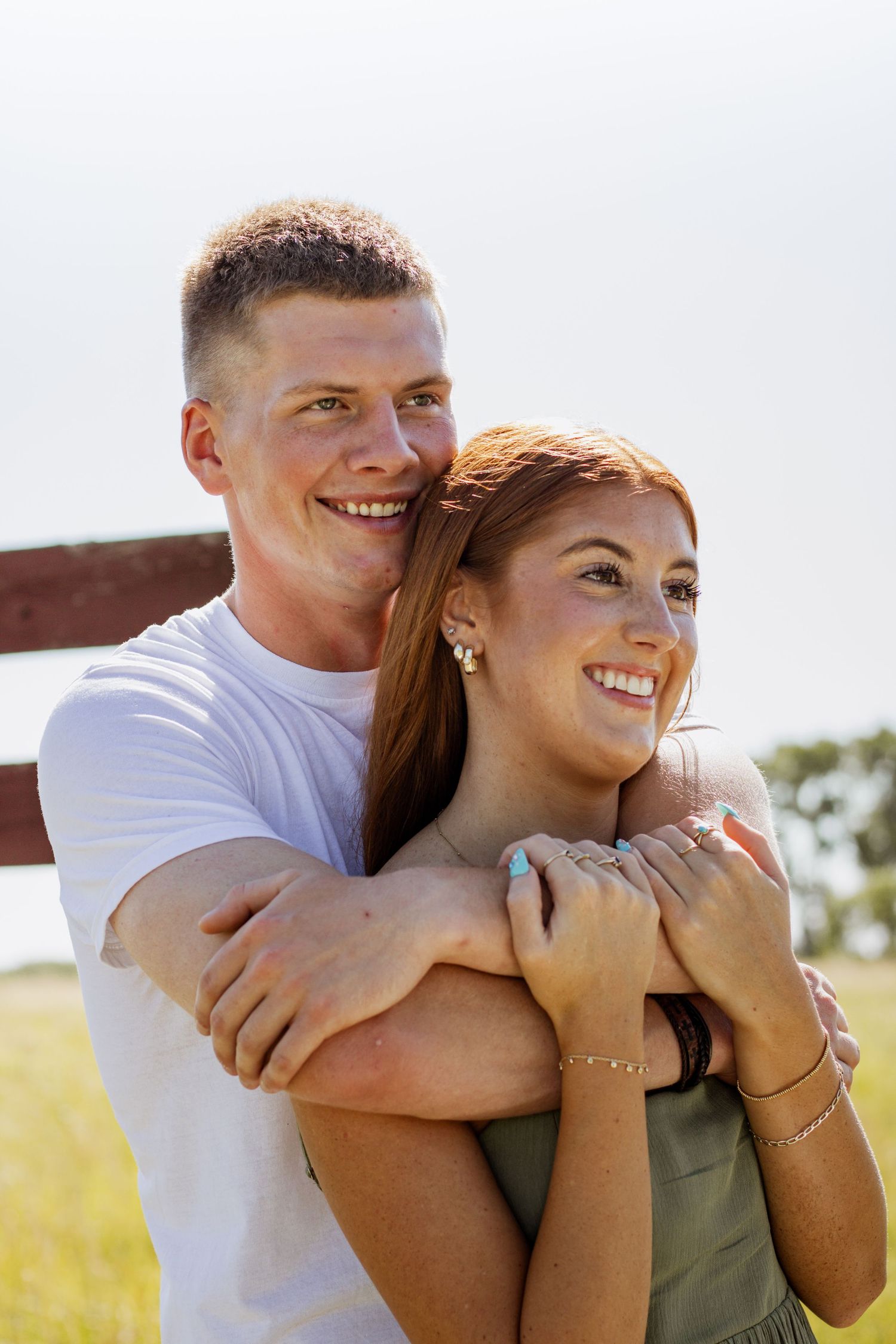 Happy young couple embracing outdoors, man in white tee hugging smiling redhead woman near a fence.