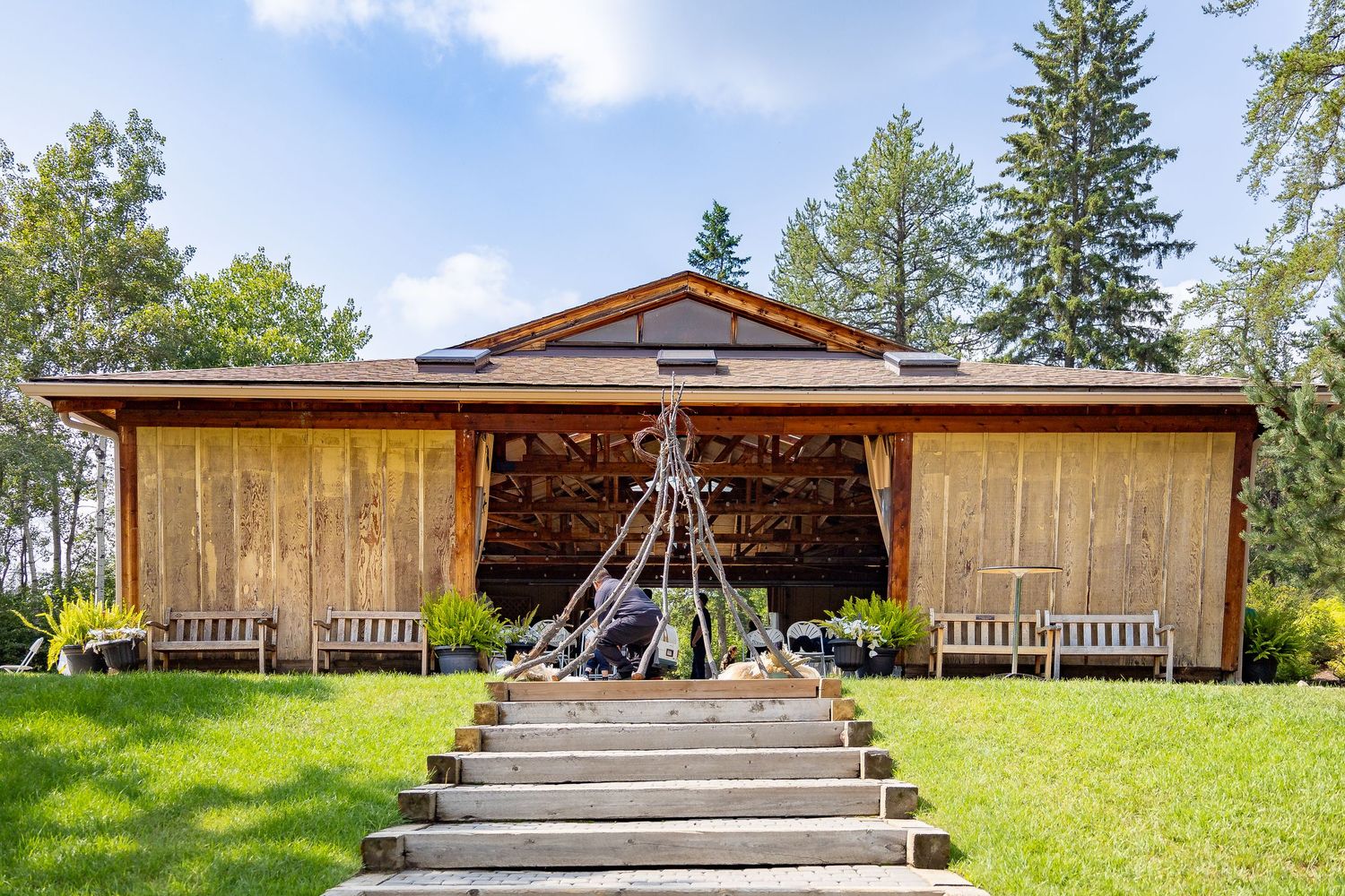 Rustic wooden wedding ceremony pavilion with steps, benches, and teepee decoration surrounded by trees.