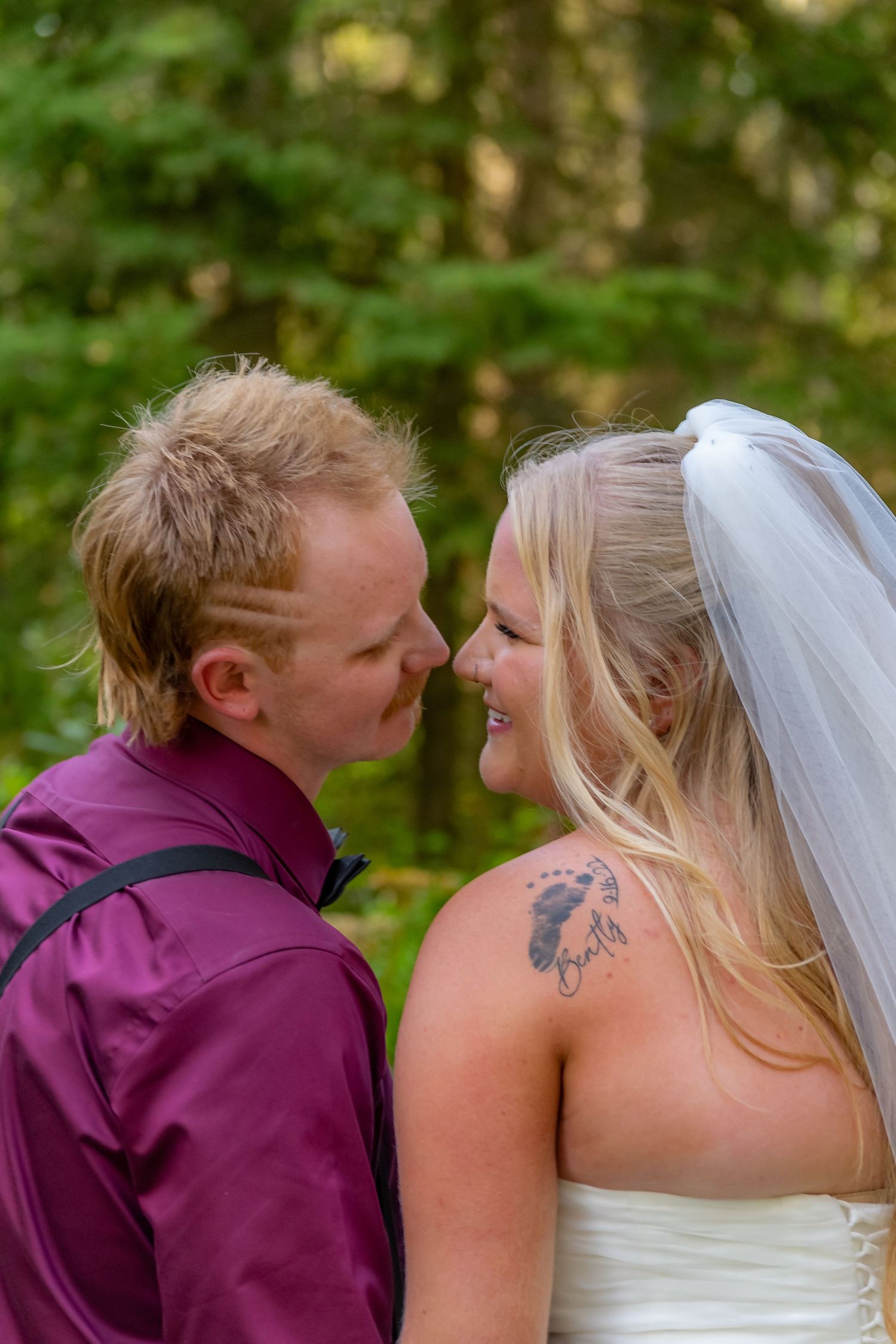 Bride and groom sharing an intimate moment smiling at each other in forest setting.