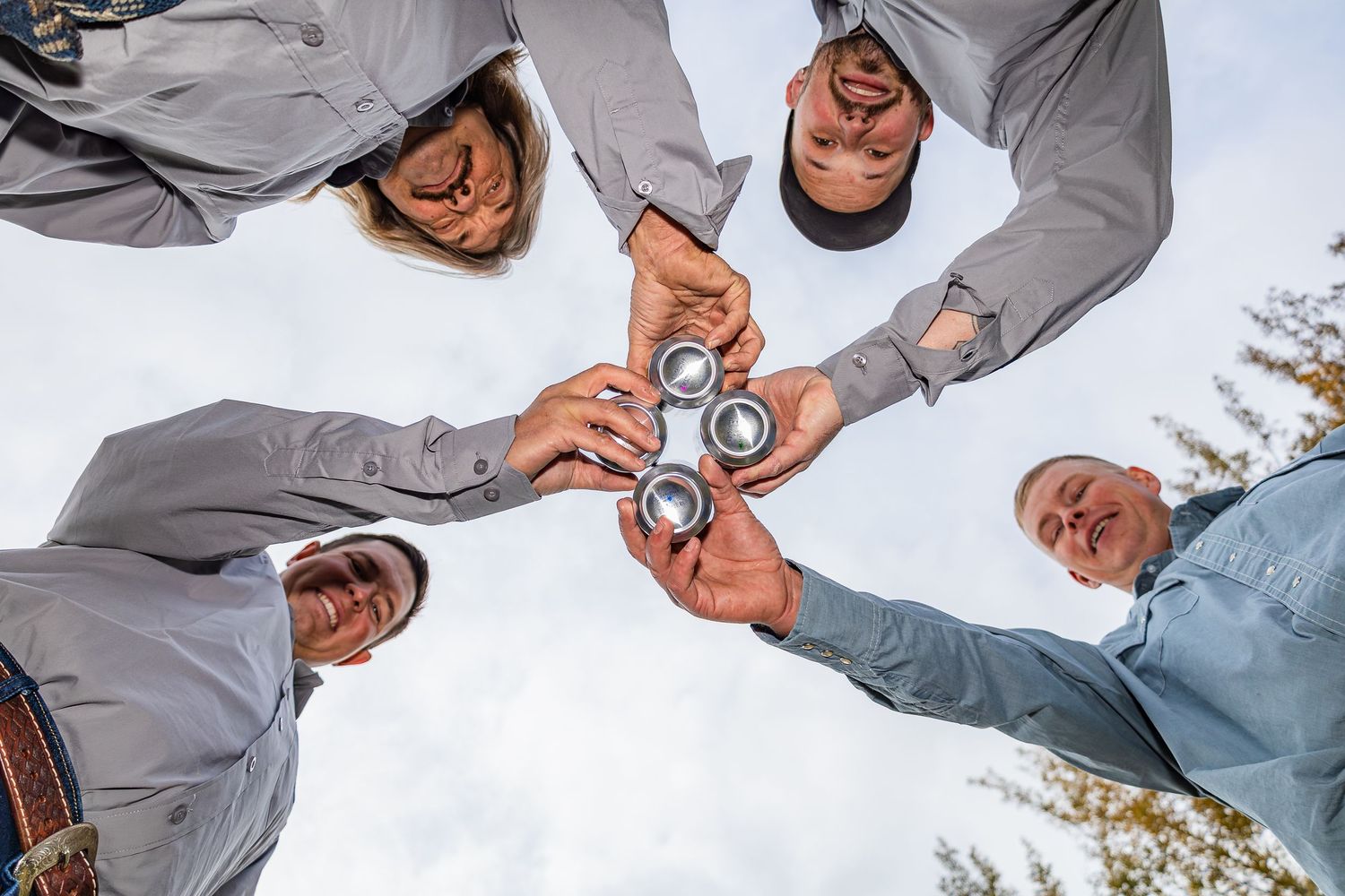 Groomsmen in gray shirts touching wedding rings together in circle from below angle.