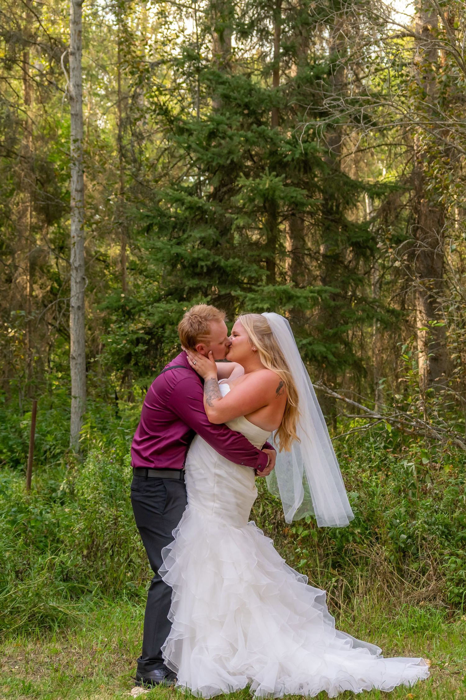 Bride and groom sharing a romantic kiss in a lush green forest setting on their wedding day.