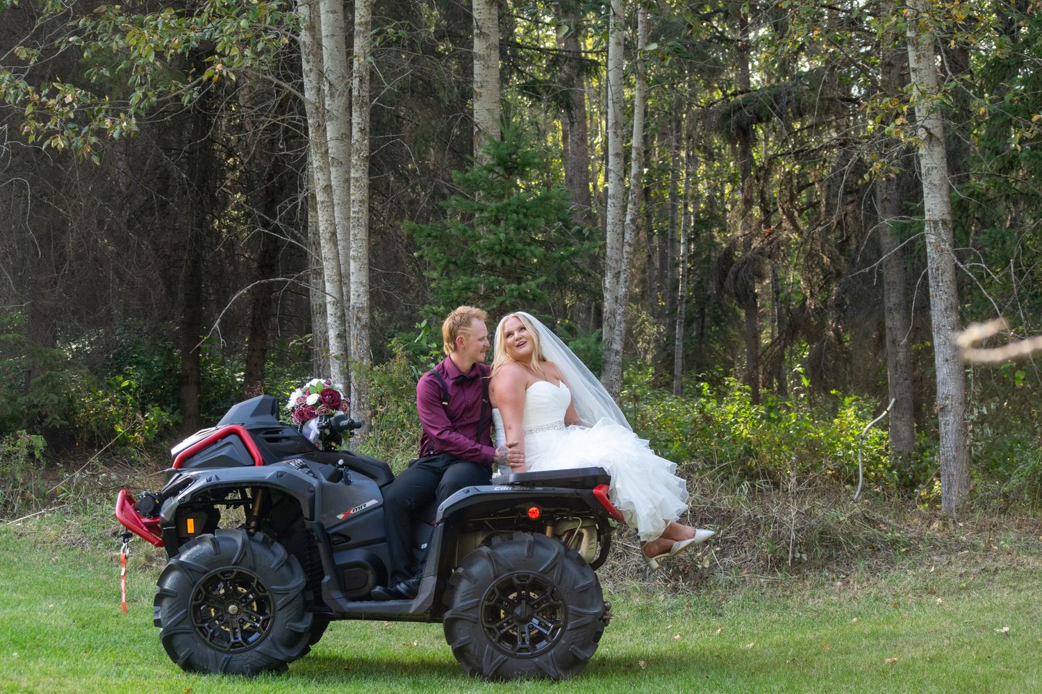 Bride and groom sitting together on a red ATV quad bike on their outdoor wedding day.