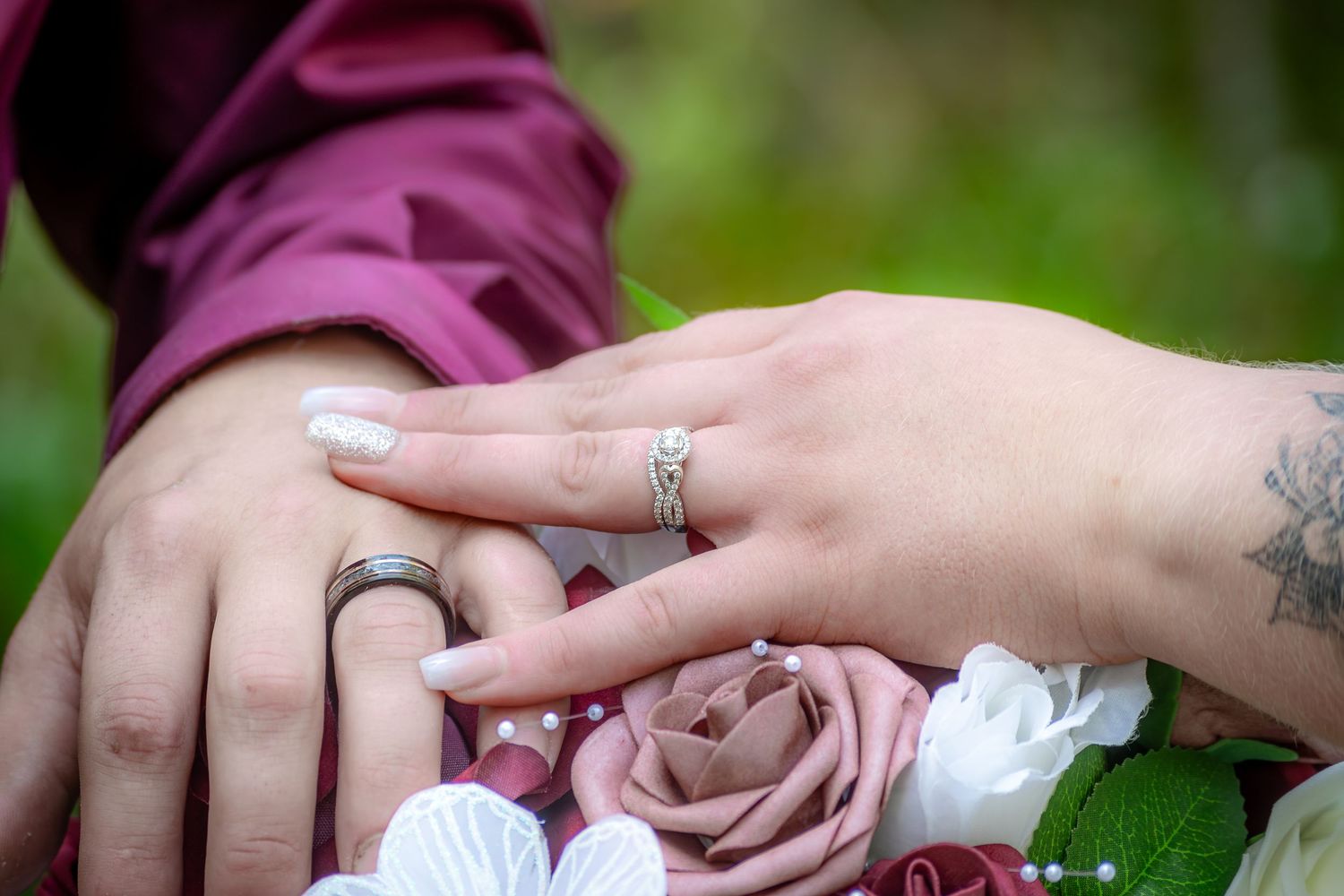 Close-up of newlyweds hands showing wedding rings with a floral bouquet featuring pink and white roses.