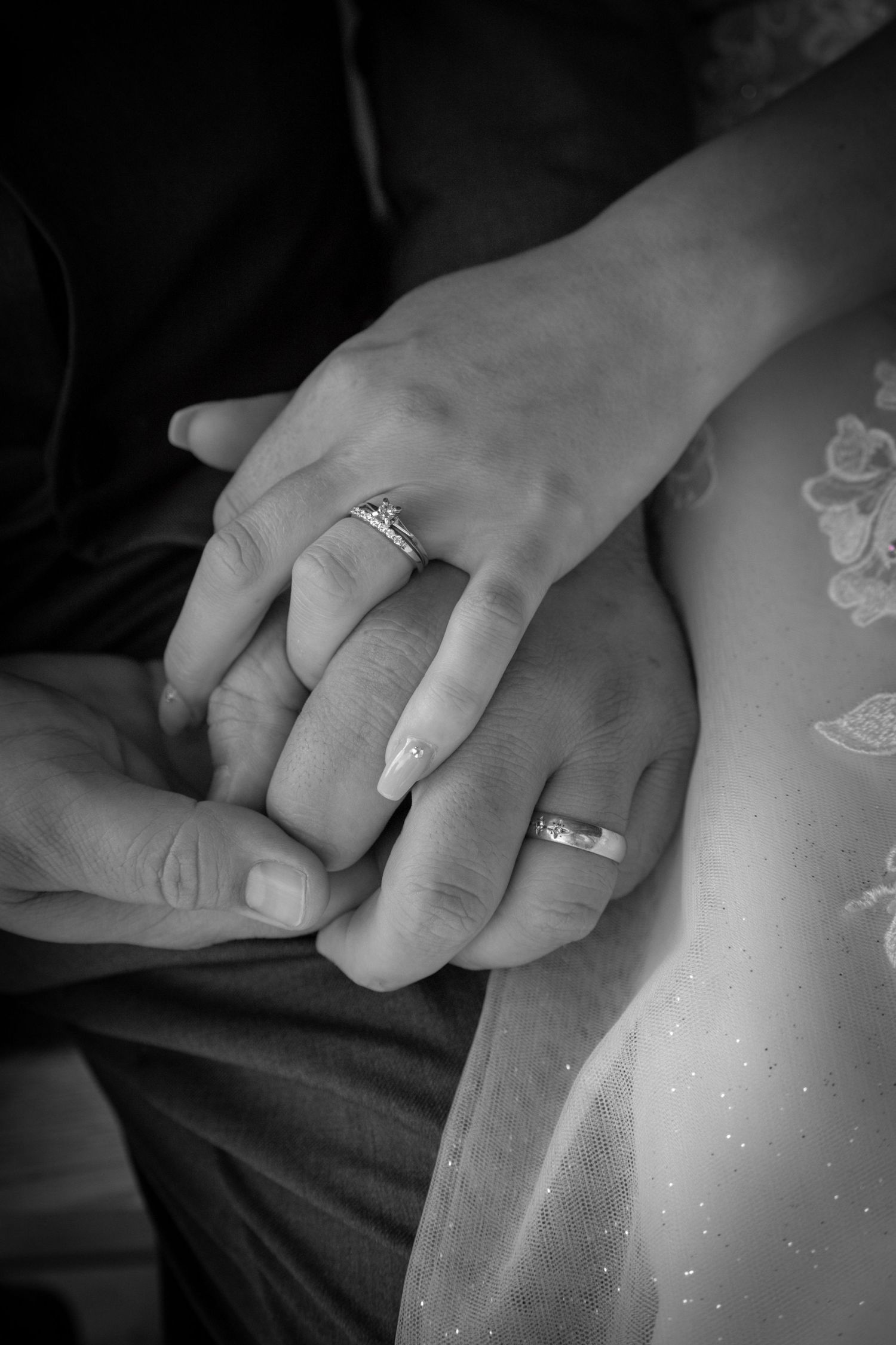 Black and white close-up of newlyweds holding hands showing wedding and engagement rings.