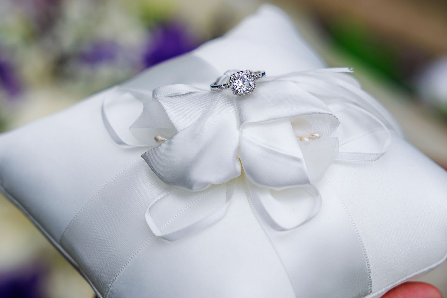 Elegant diamond engagement ring displayed on a white satin ring pillow with ribbon bow detail.