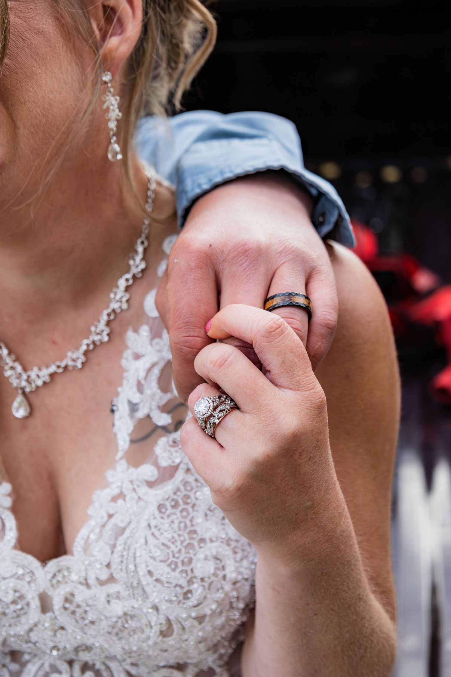 Close-up of bride and groom holding hands showing wedding rings, bride wearing lace gown and diamond jewelry.