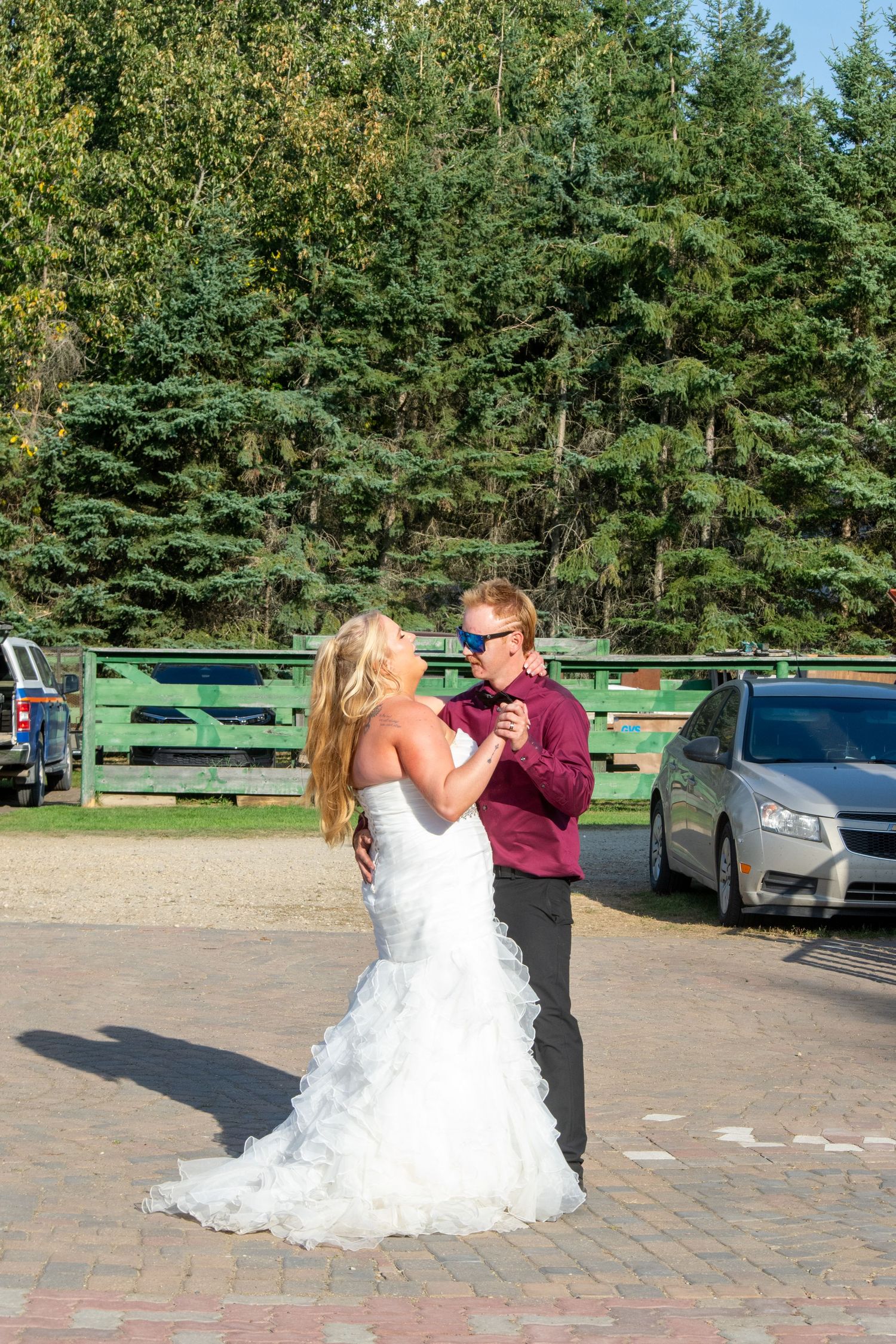Bride and groom sharing their first dance outdoors on a paved area with trees in background.