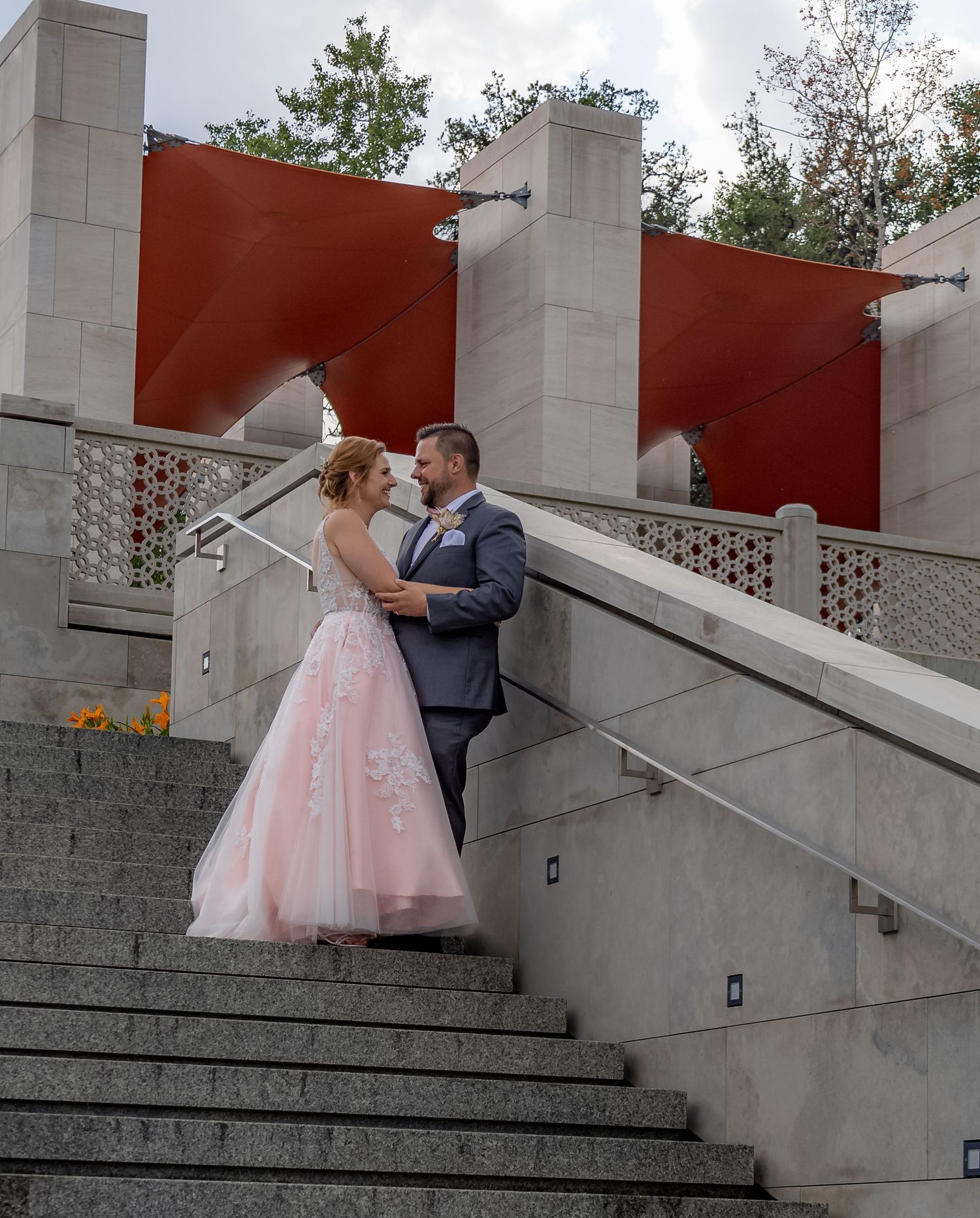 Bride and groom share an intimate moment on stone steps near a modern venue.