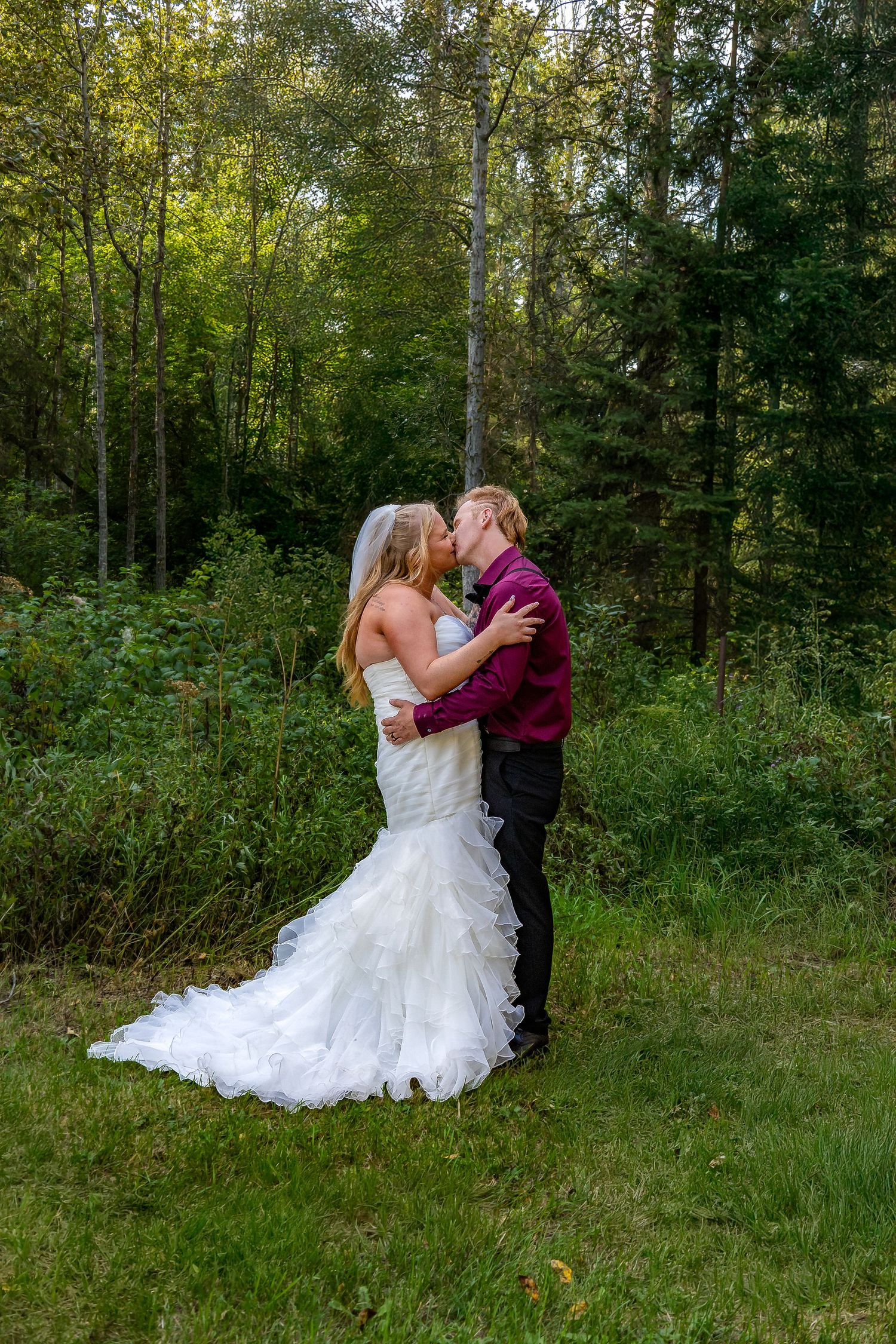 Bride and groom sharing a passionate kiss in a lush green forest on their wedding day.