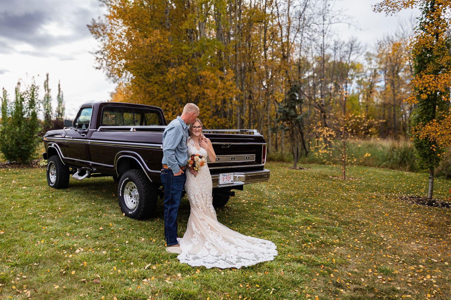 Bride and groom posing beside vintage dark brown pickup truck in autumn setting.