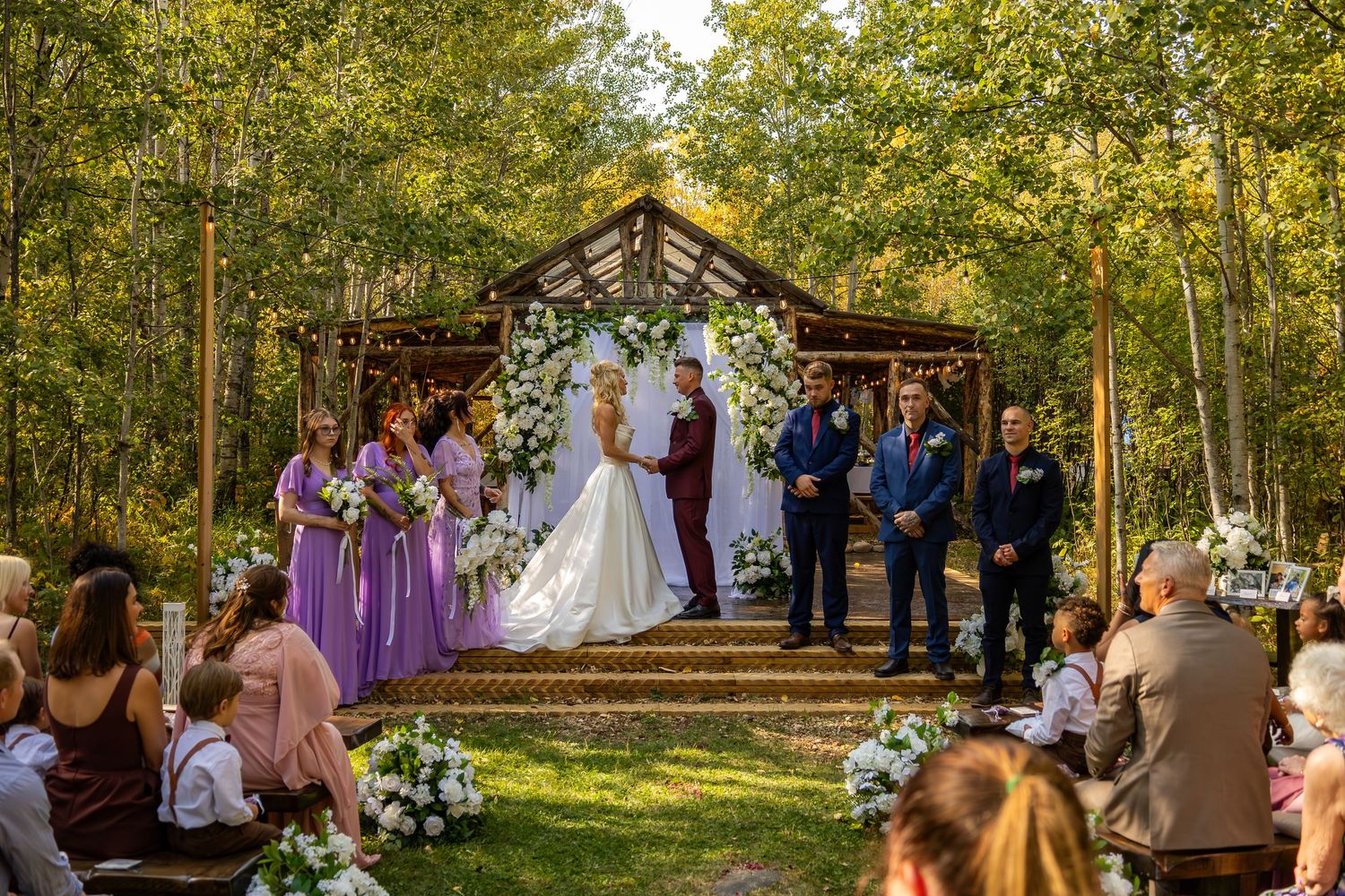 Outdoor fall wedding ceremony under a white floral arch in a rustic wooden gazebo surrounded by golden aspen trees.