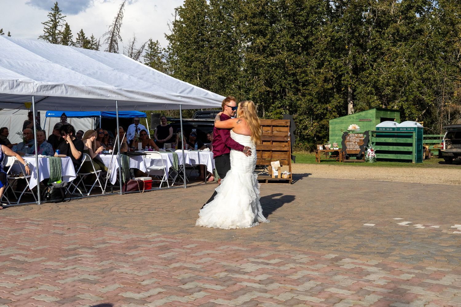 Bride and groom dancing outdoors near a white tent with wedding guests seated at tables.
