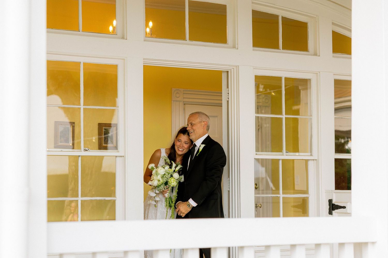 Bride and groom pose romantically in a white-framed doorway with yellow walls during their wedding day.