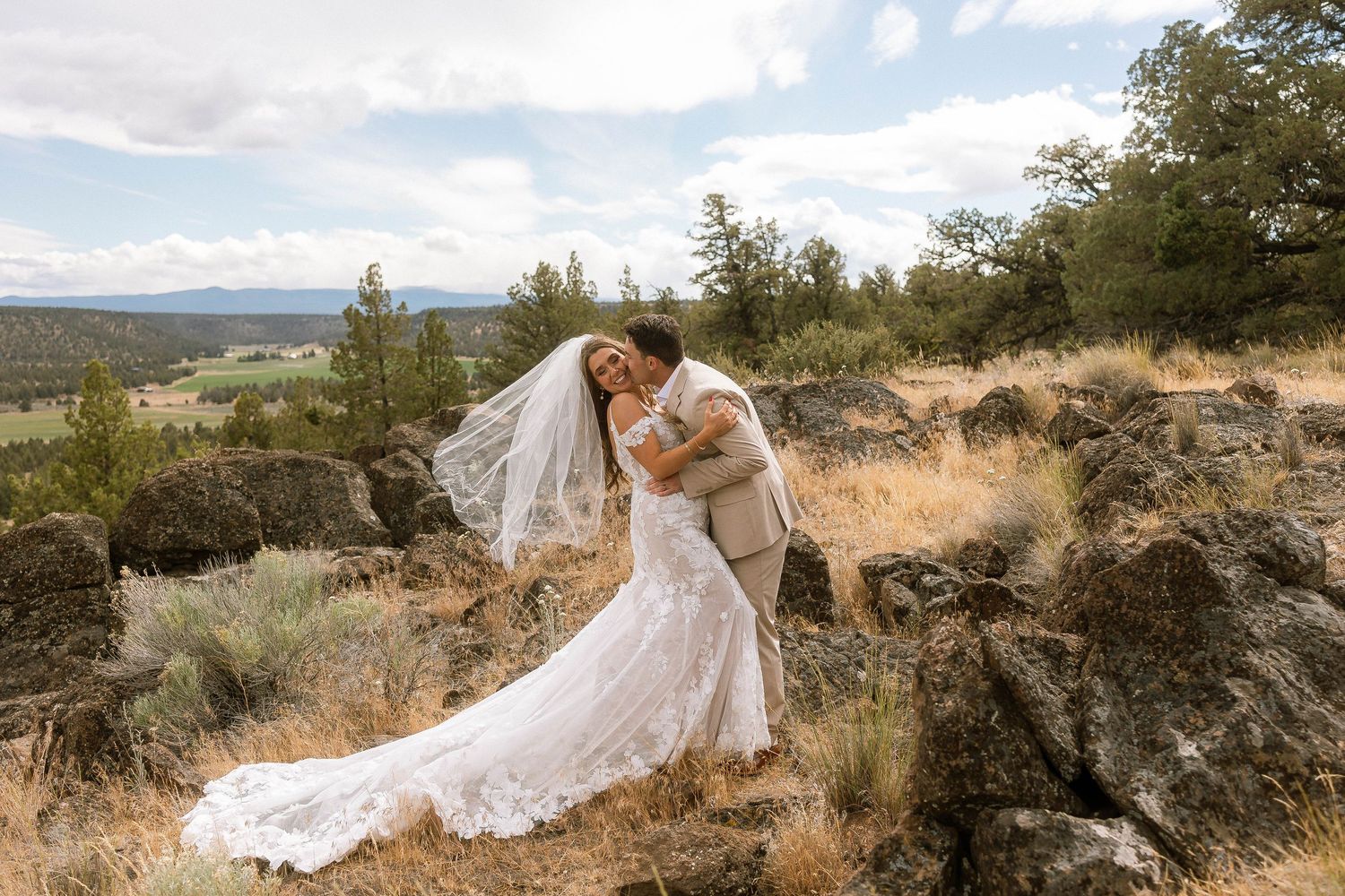 Bride and groom share romantic kiss among rocky landscape with scenic valley views on their wedding day.