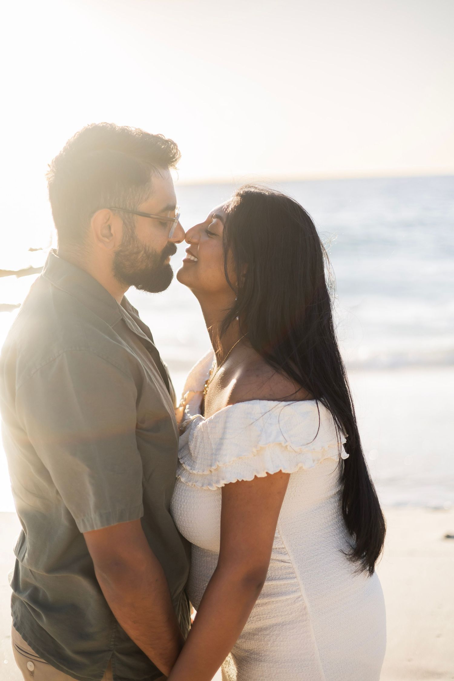Couple sharing a romantic moment on a sunlit beach, nearly kissing while holding each other close.