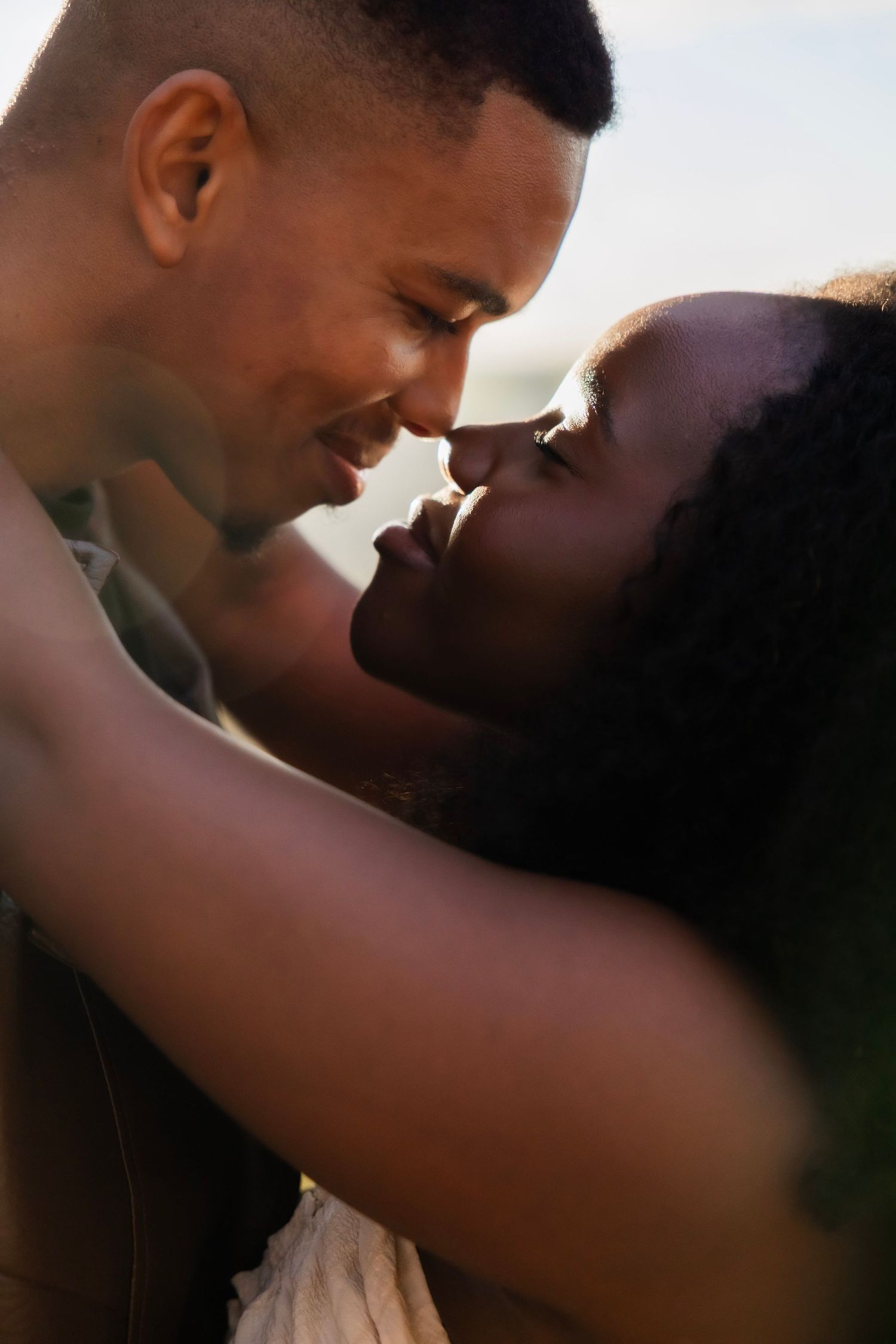 A romantic couple sharing an intimate moment, touching foreheads and smiling in warm golden sunlight.