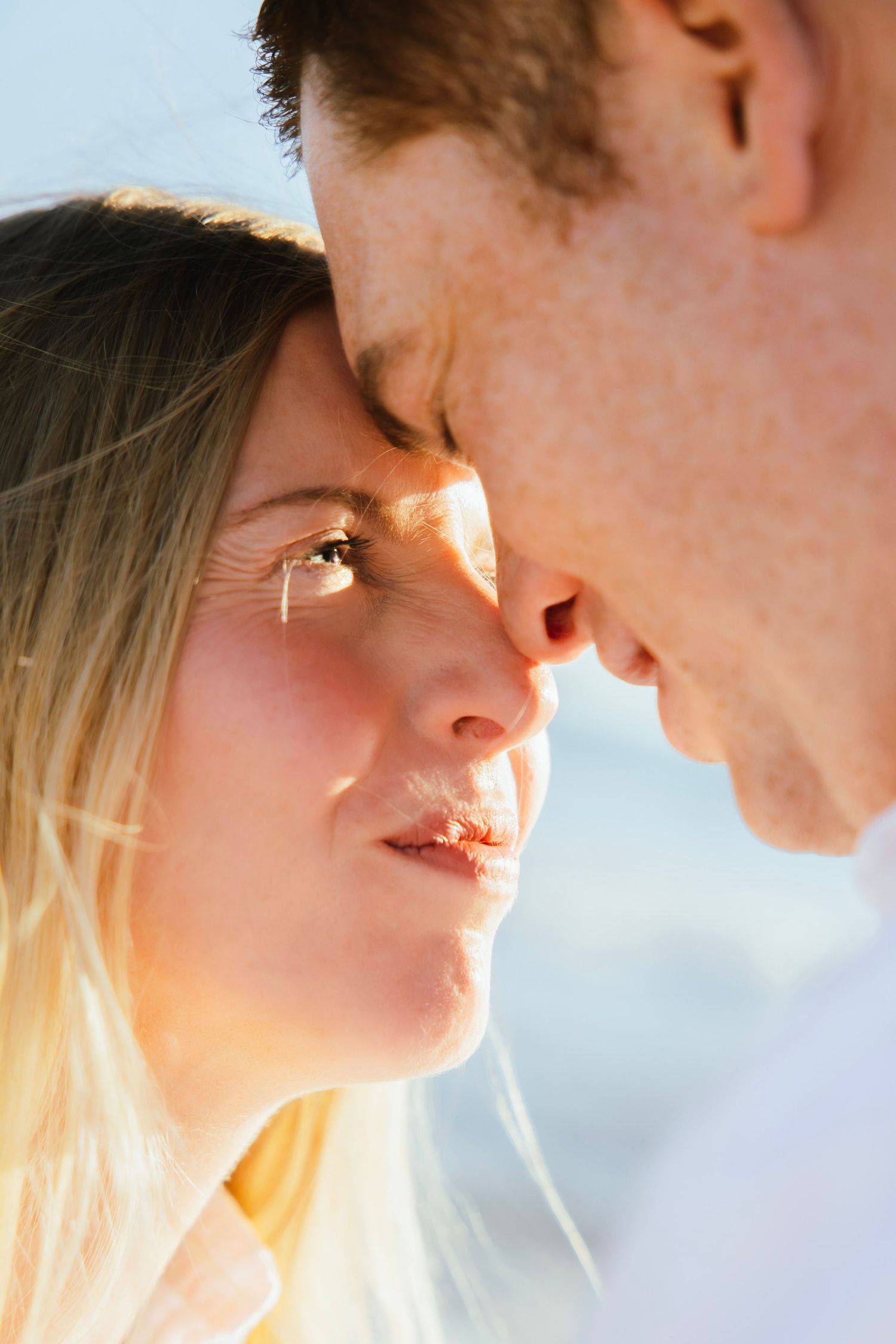 Romantic close-up of couple facing each other, nearly kissing in warm golden sunlight.