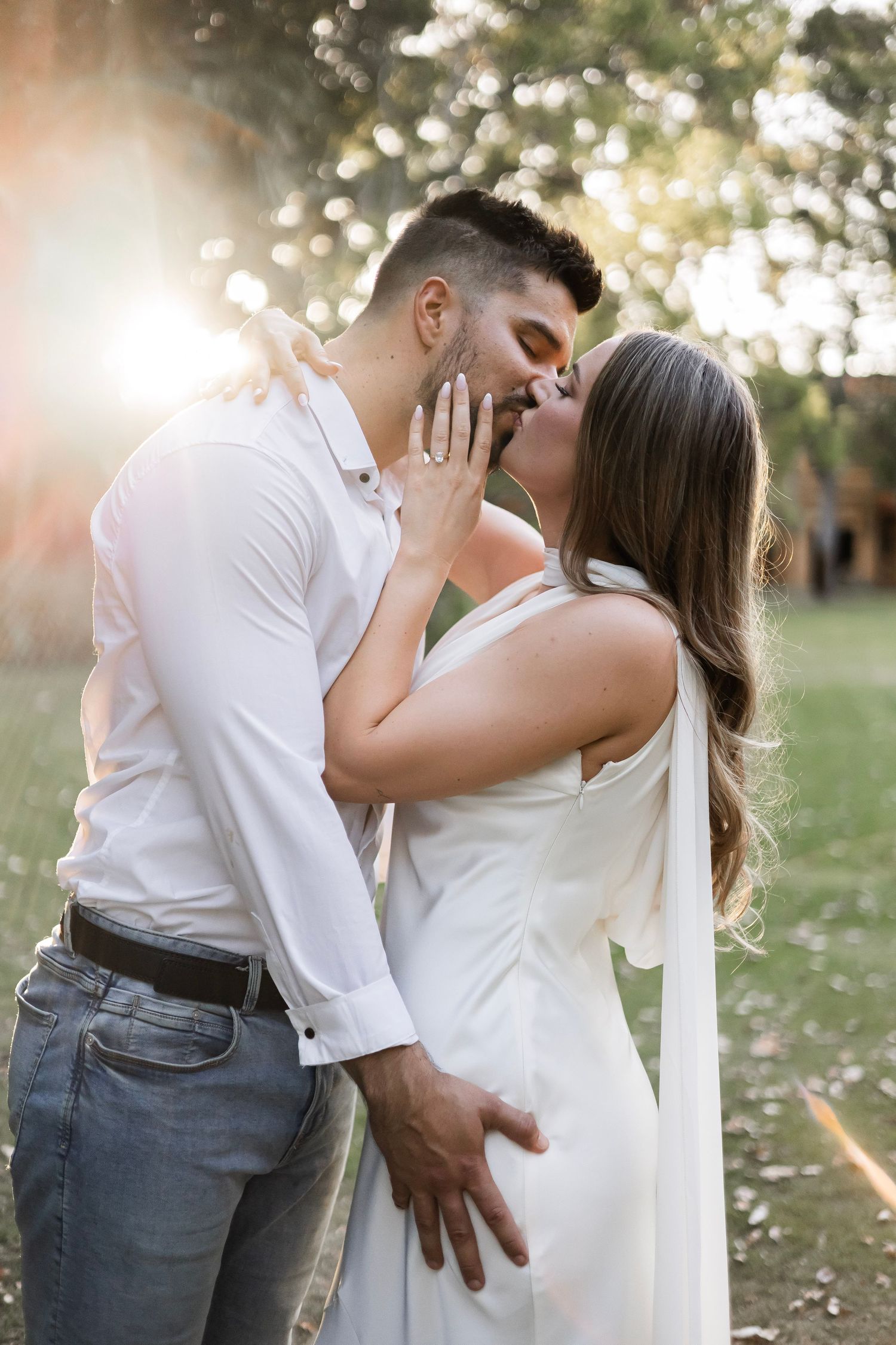Couple kissing romantically with golden sun flare in an outdoor garden setting.
