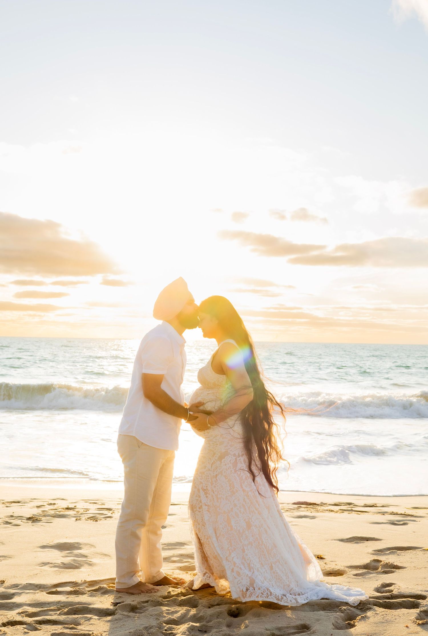 Expecting couple sharing a romantic moment at sunset on a sandy beach.