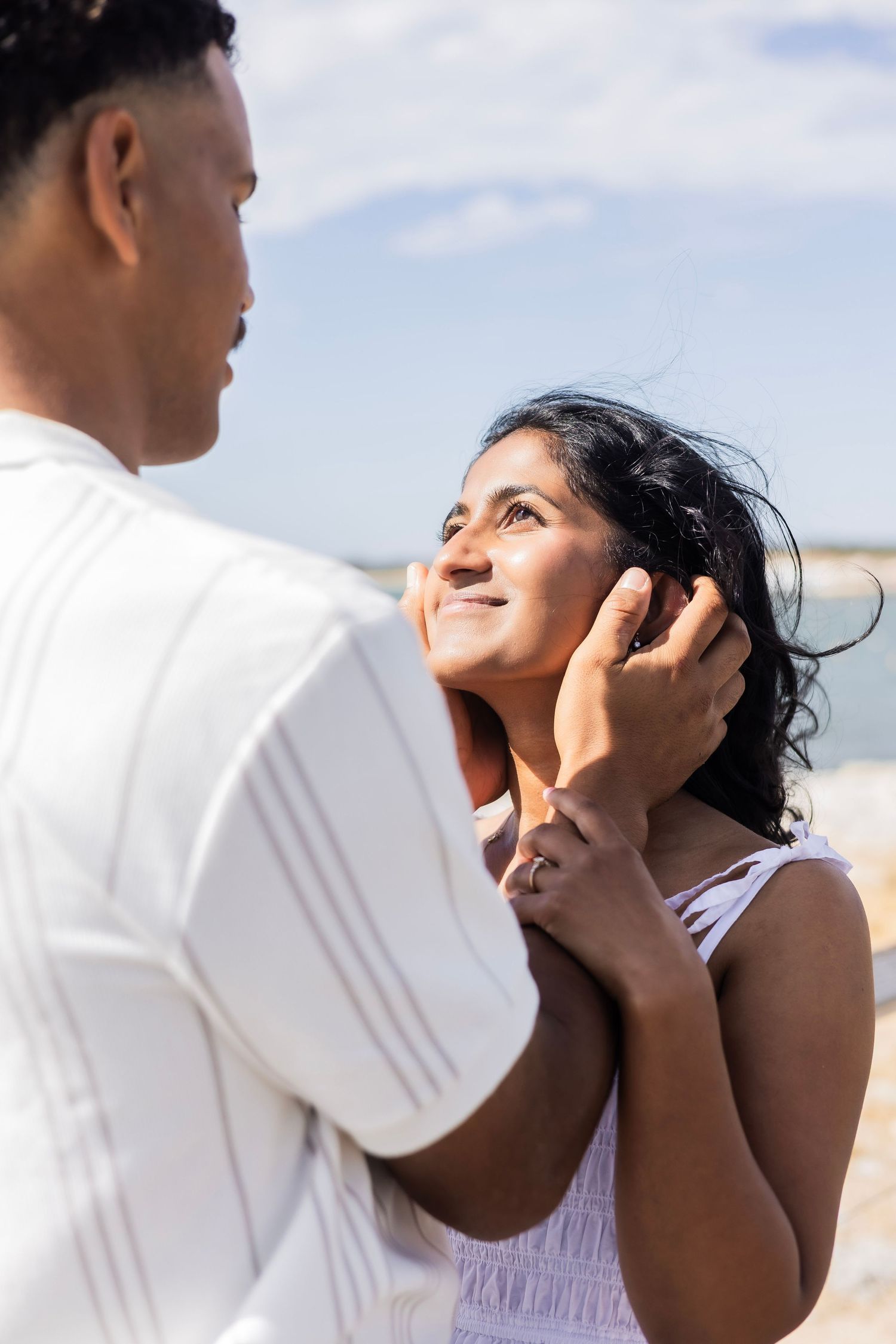 Woman smiling up at man on a sunny beach as he gently holds her face in his hands.