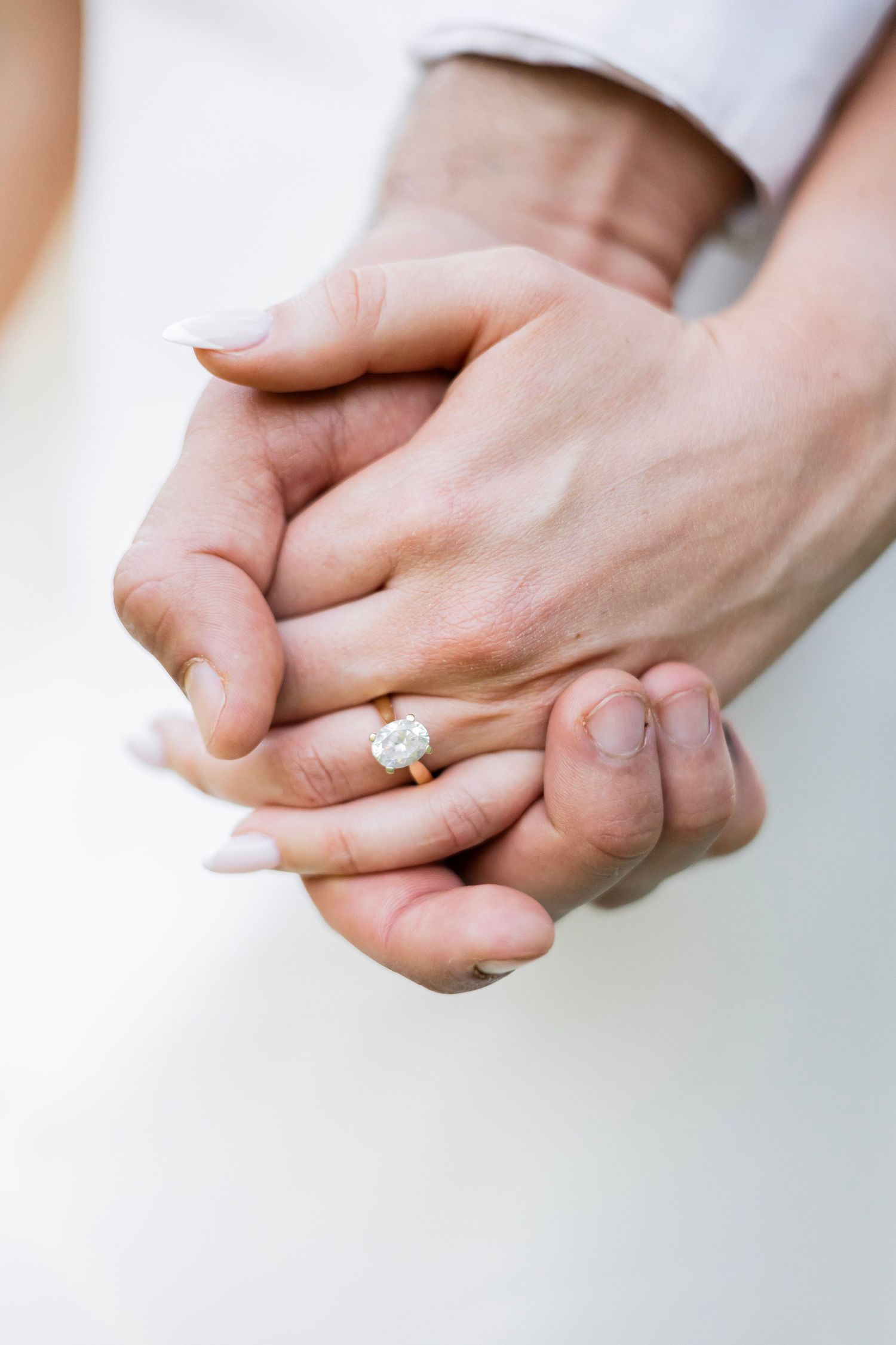 Close-up of couple holding hands showing diamond engagement ring on womans finger with manicured nails.