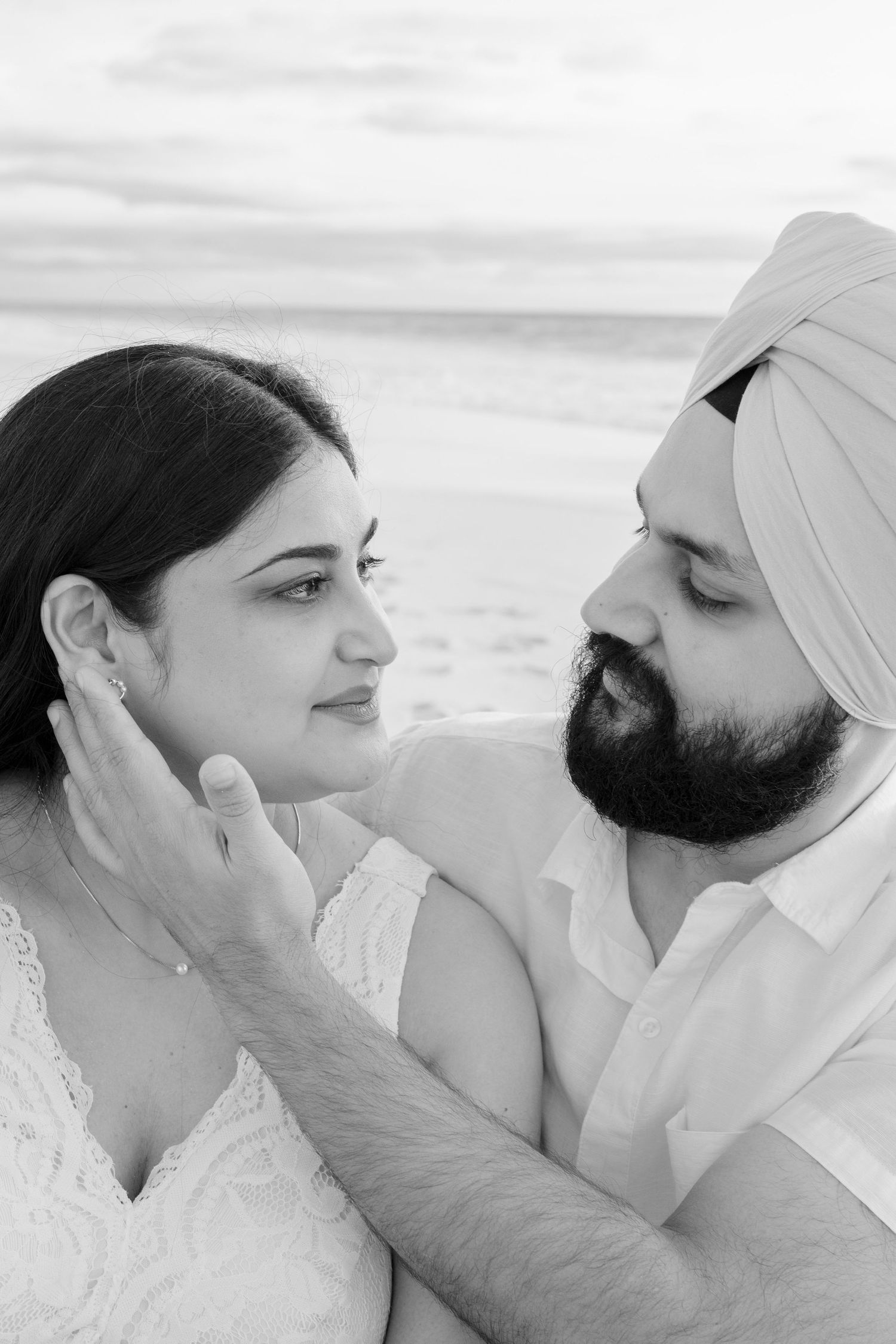 Black and white portrait of expecting couple sharing a tender moment on the beach.