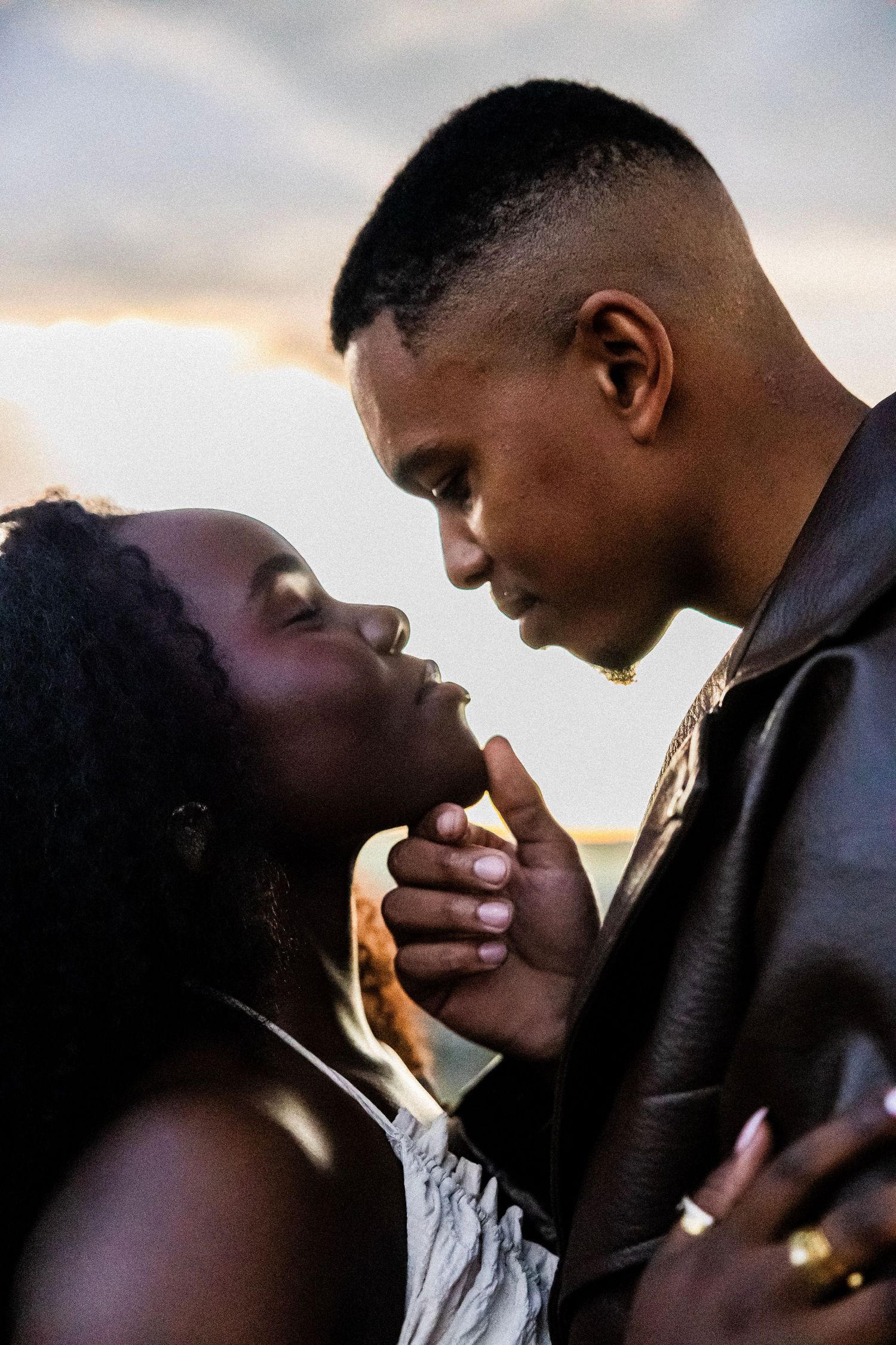 A romantic couple shares an intimate moment, the man tenderly holding the woman's chin as they lean in close.