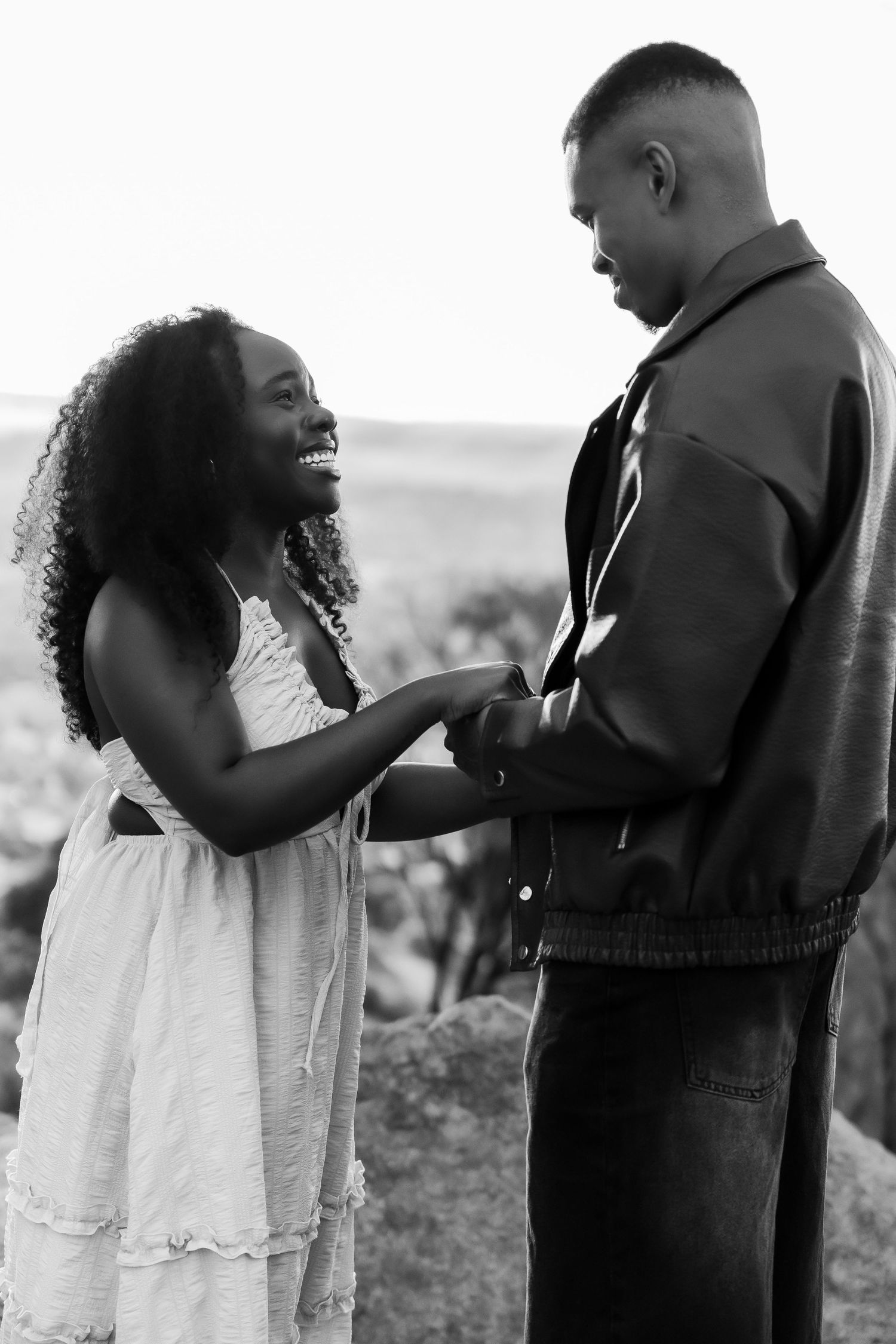 A joyful Black couple holds hands and shares a laugh in a romantic black and white outdoor portrait photo.