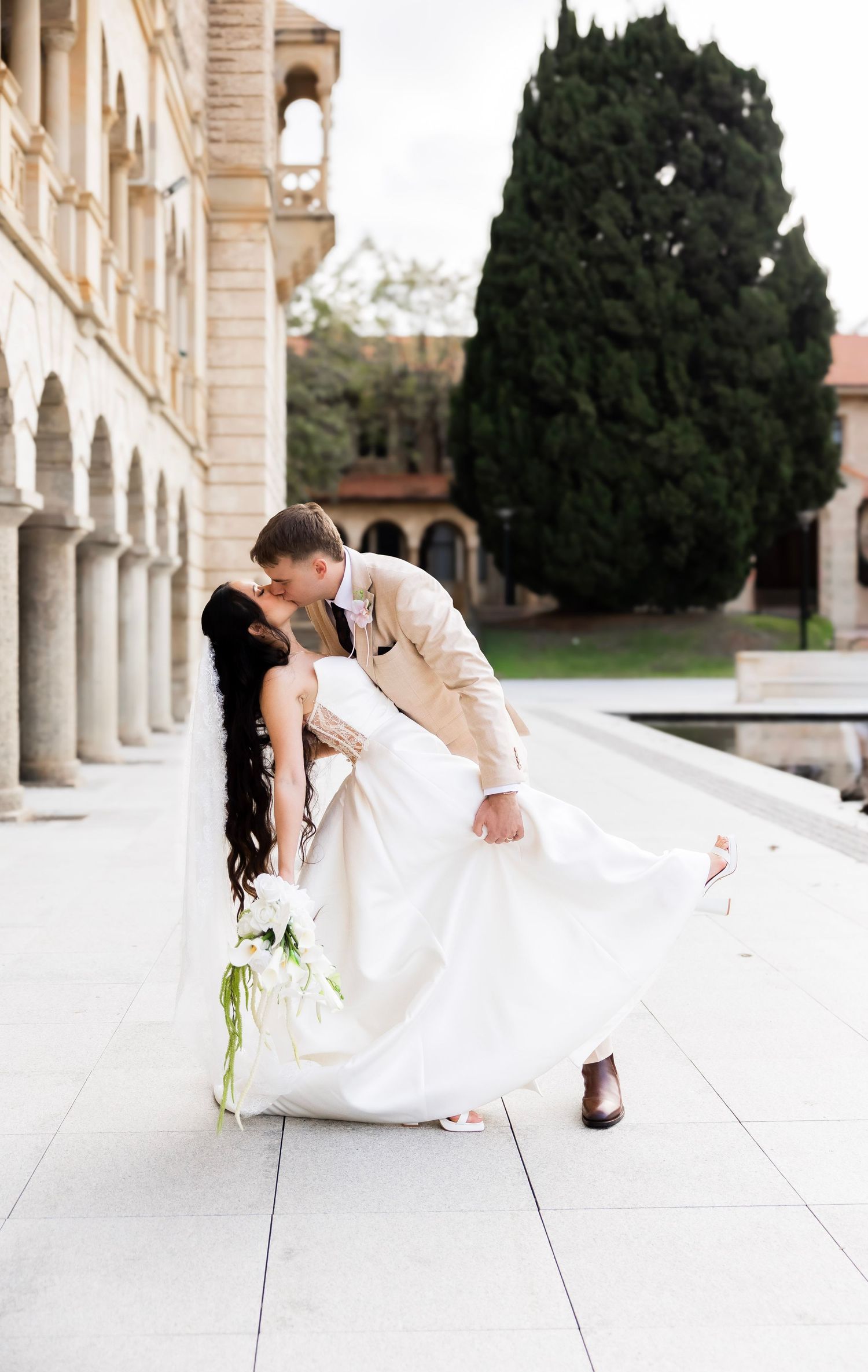 Groom dips bride for a kiss outside historic building on wedding day.