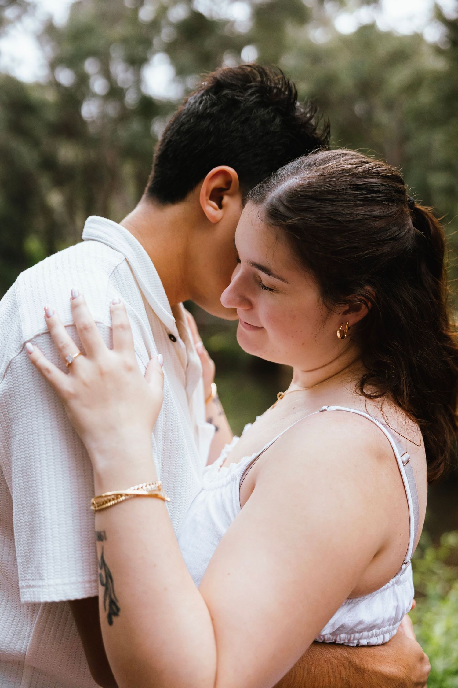 Couple sharing an intimate moment outdoors, woman smiling softly with eyes closed in nature.