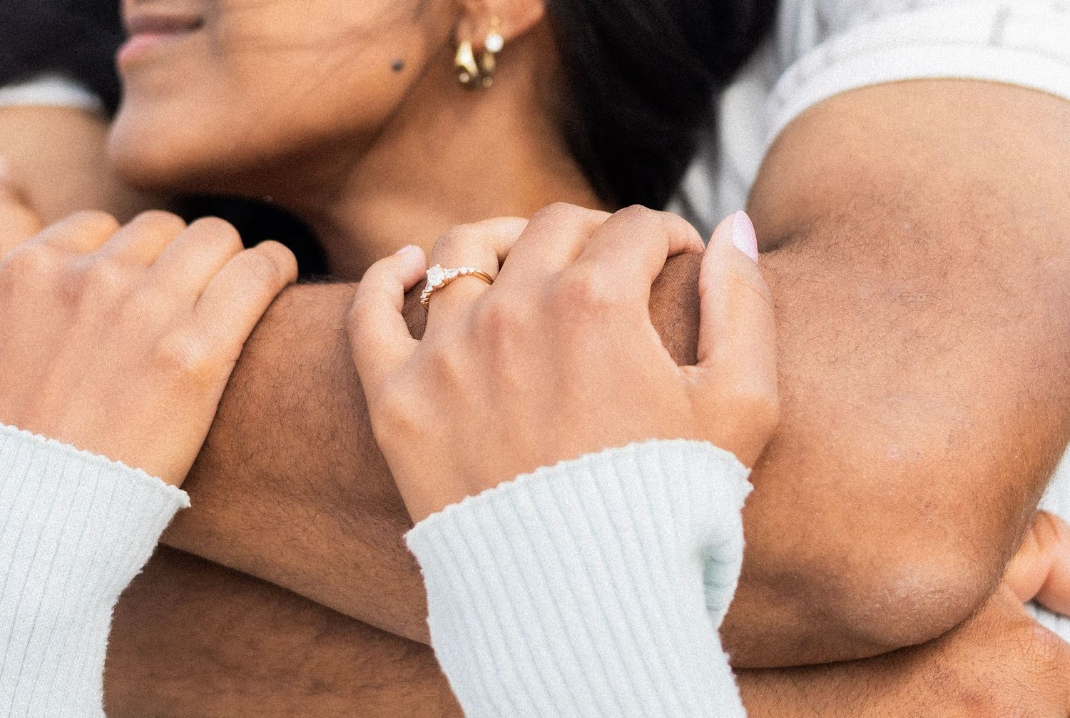 Color close-up of woman with engagement ring embracing mans arm affectionately outdoors.