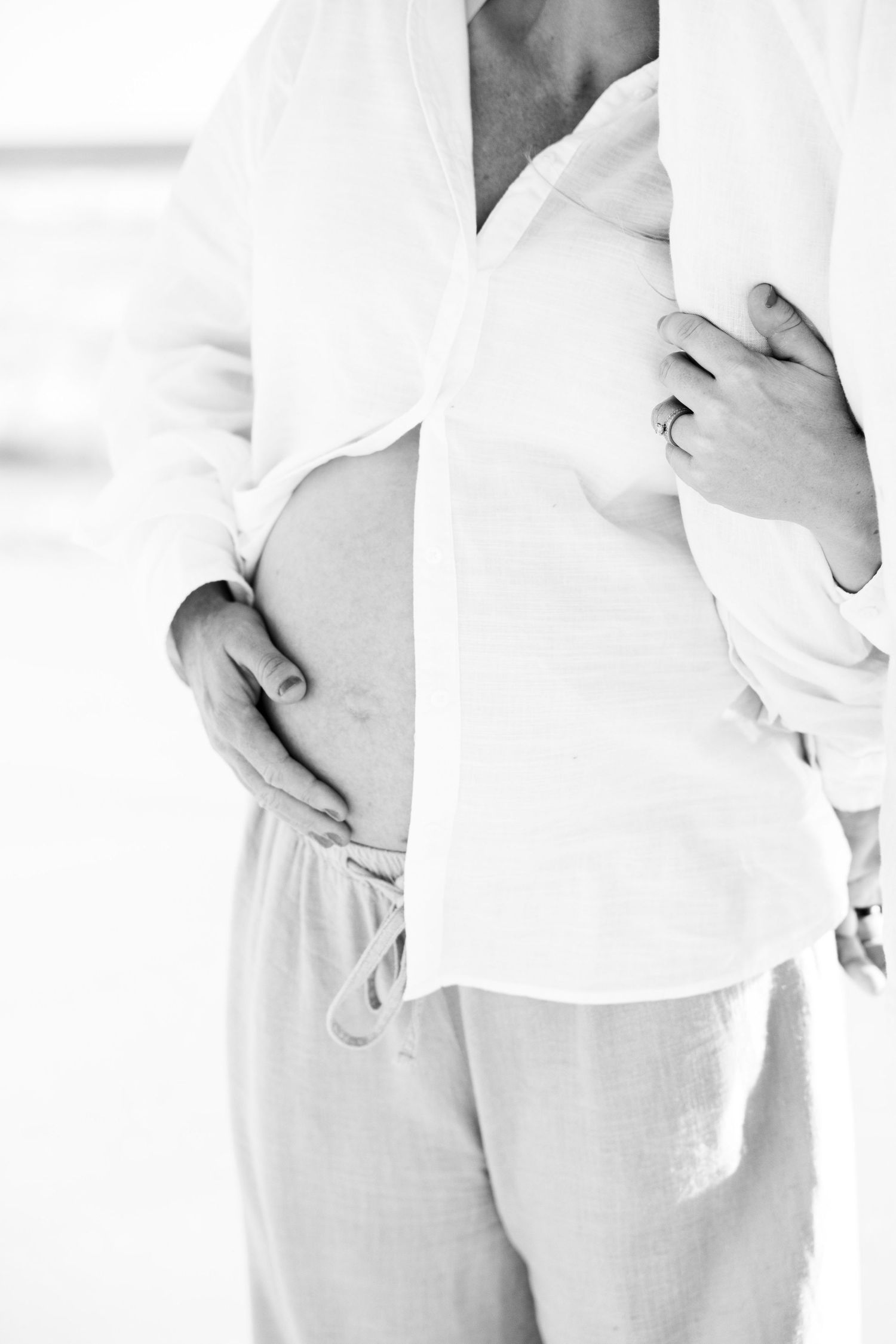 Black and white close-up of pregnant woman's bare belly held by partner's hands.