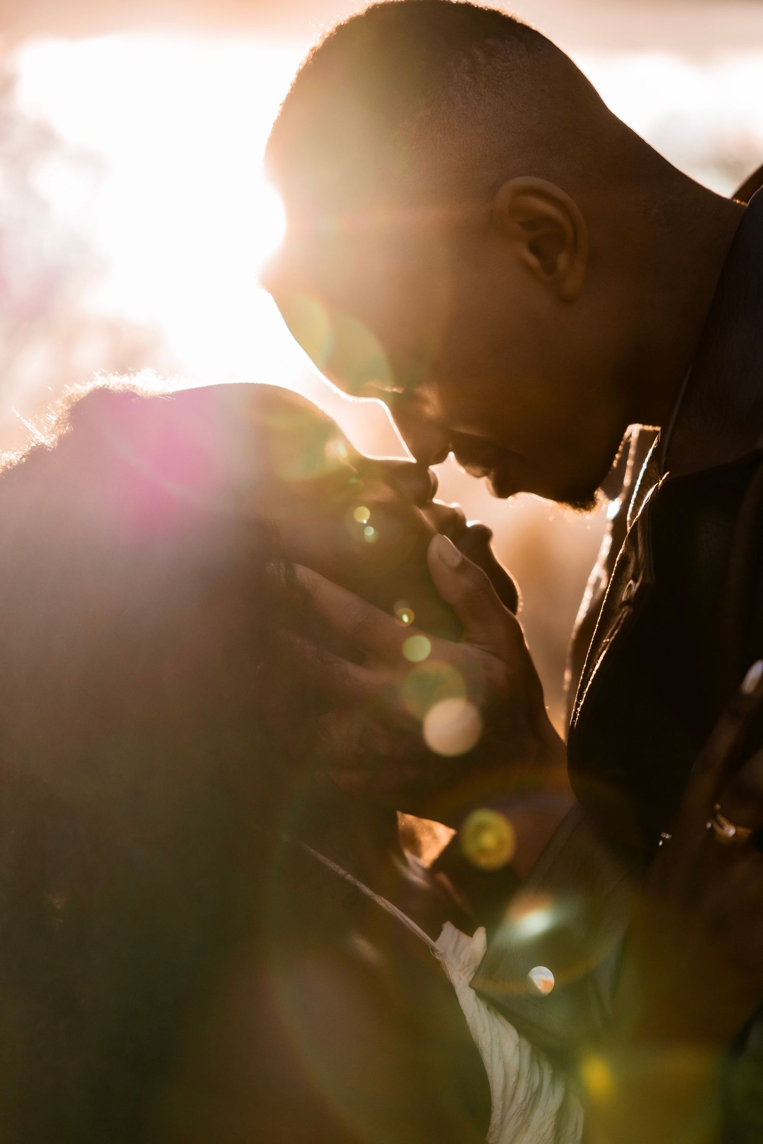 A couple shares an intimate moment at golden hour, their foreheads touching as warm sunlight creates a beautiful lens flare.